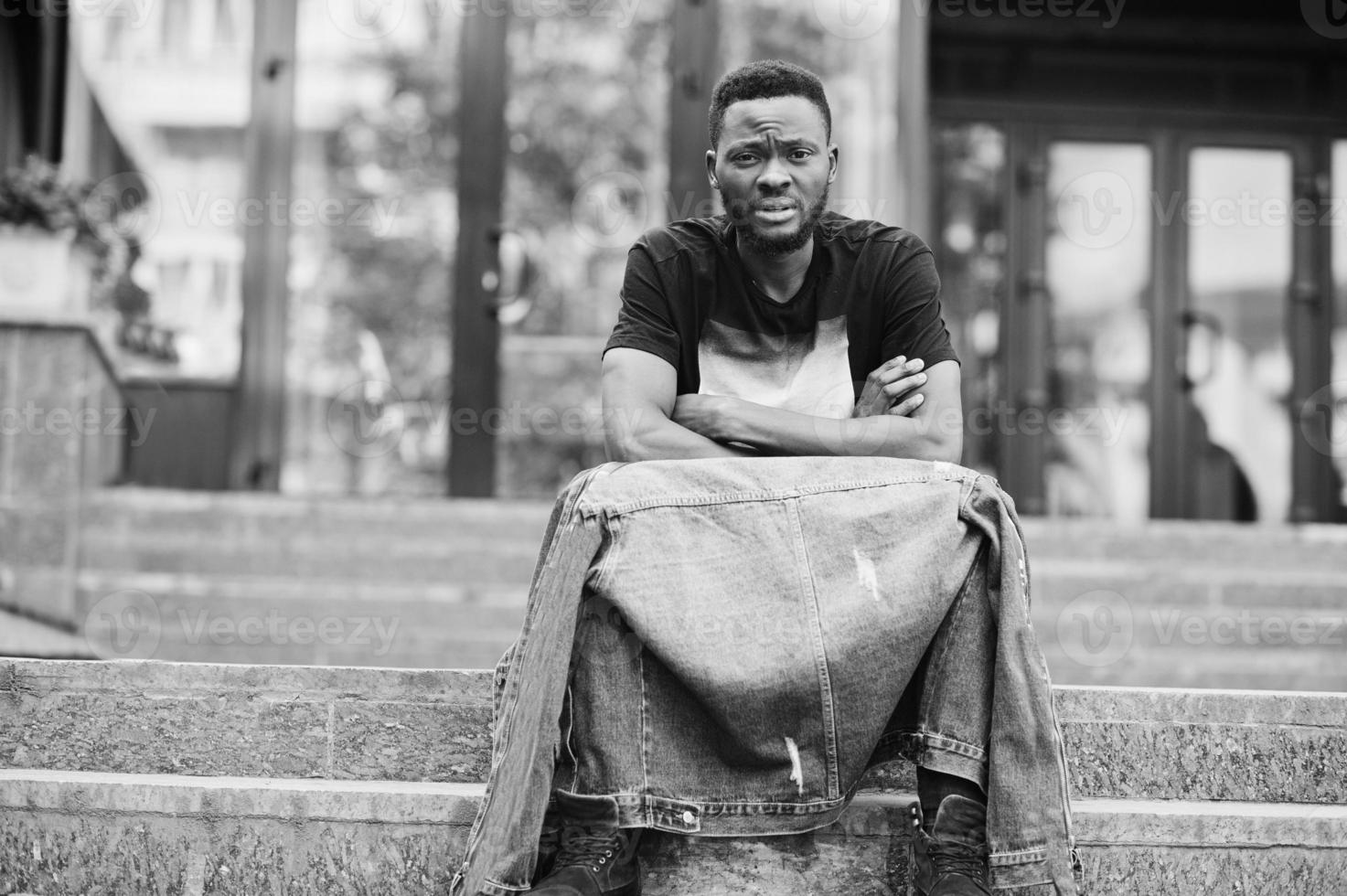 ung attraktiv seriös afrikansk amerikansk man modell. modern stilig kille i jeansjacka sitter på stadsgatan. foto