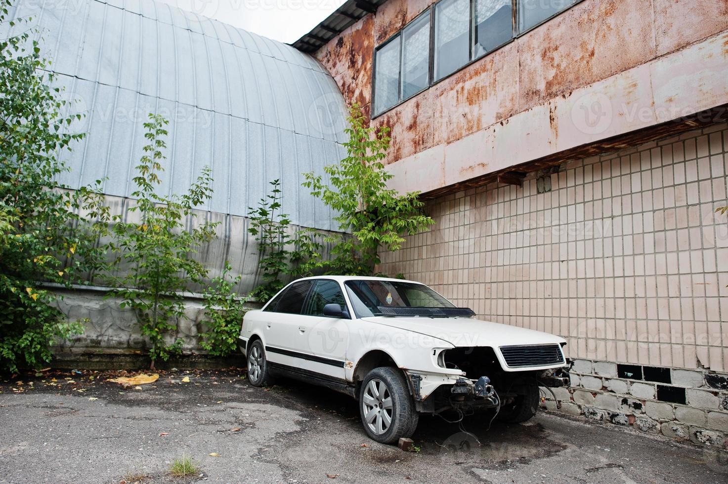 vit bil demonterad utan strålkastare, stötfångare och egine på gammal fabrik. foto