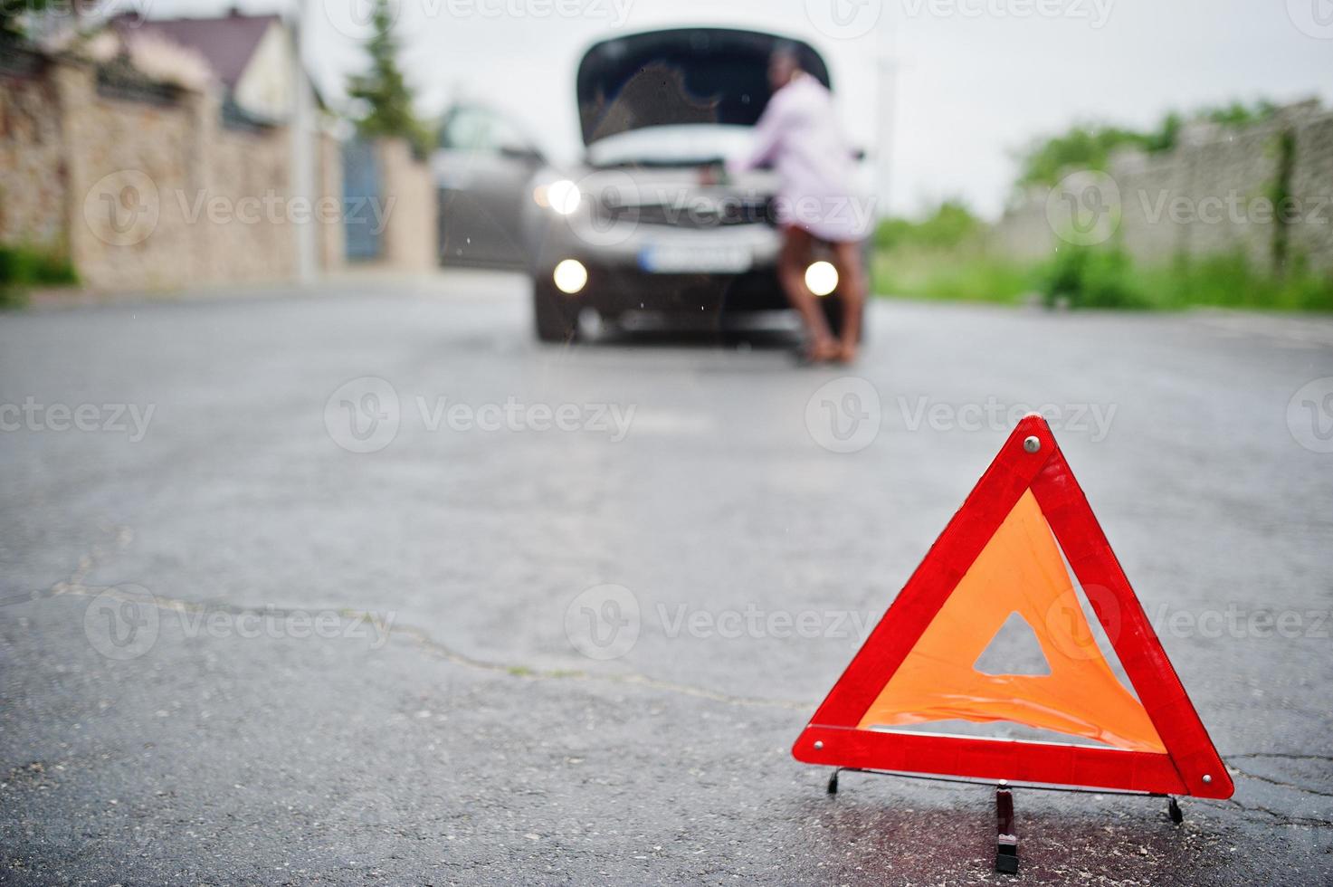 ung ledsen afrikansk kvinna står med nödtriangel mot bil med kåpa. transport, fordon problem och haverier koncept. foto