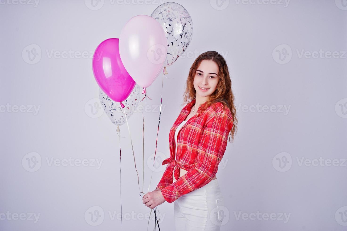 ung flicka i röd rutig skjorta och vita byxor med ballonger mot vit bakgrund på studio. foto