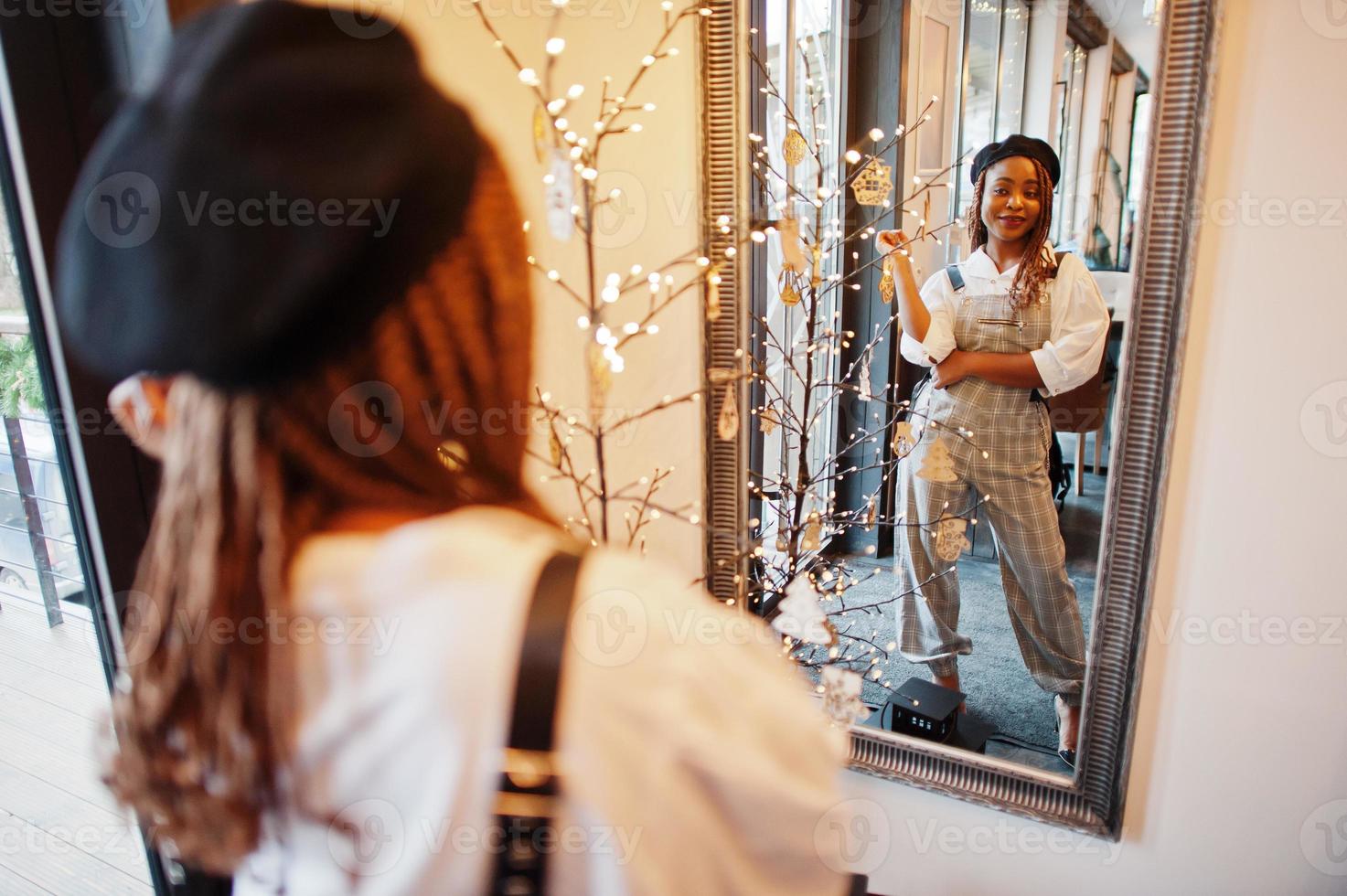 afrikansk amerikansk kvinna i overall och basker mot spegel i mjukt ljus rum. foto