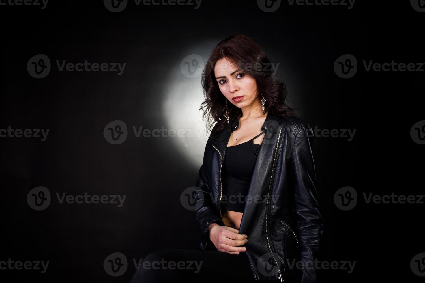 studio porträtt av sexig brunett tjej i svart skinnjacka mot svart bakgrund. foto