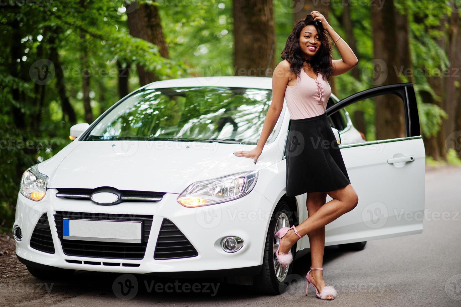 afrikansk amerikansk kvinna poserade mot vit bil i skogsväg. foto