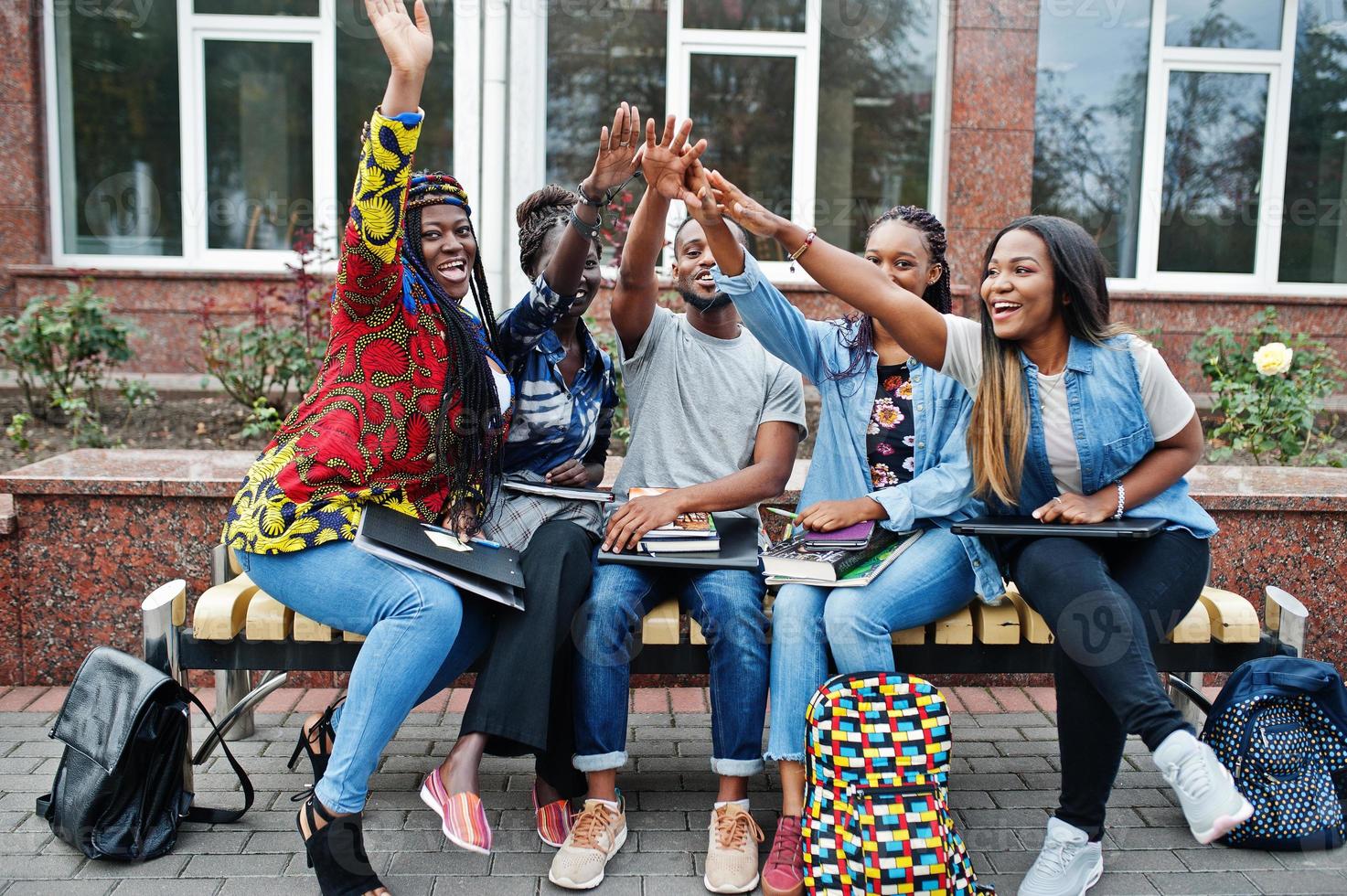 grupp på fem afrikanska högskolestudenter som spenderar tid tillsammans på campus på universitetsgården. svarta afro vänner studerar vid bänken med skolsaker, bärbara datorer anteckningsböcker. foto