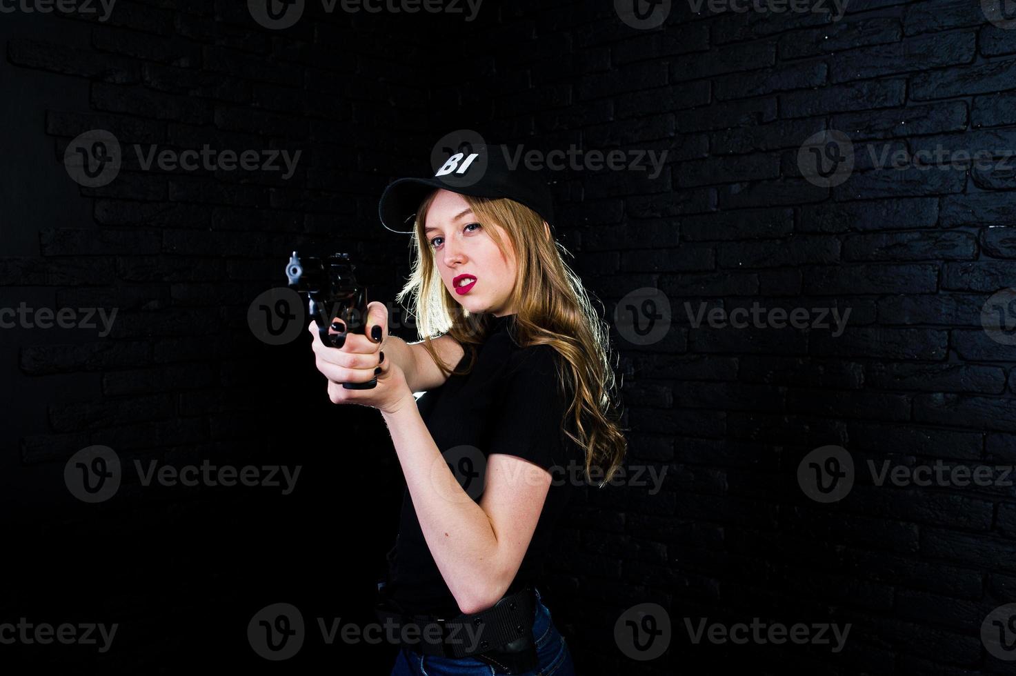 FBI kvinnlig agent i mössa och med pistol i studio mot mörk tegelvägg. foto
