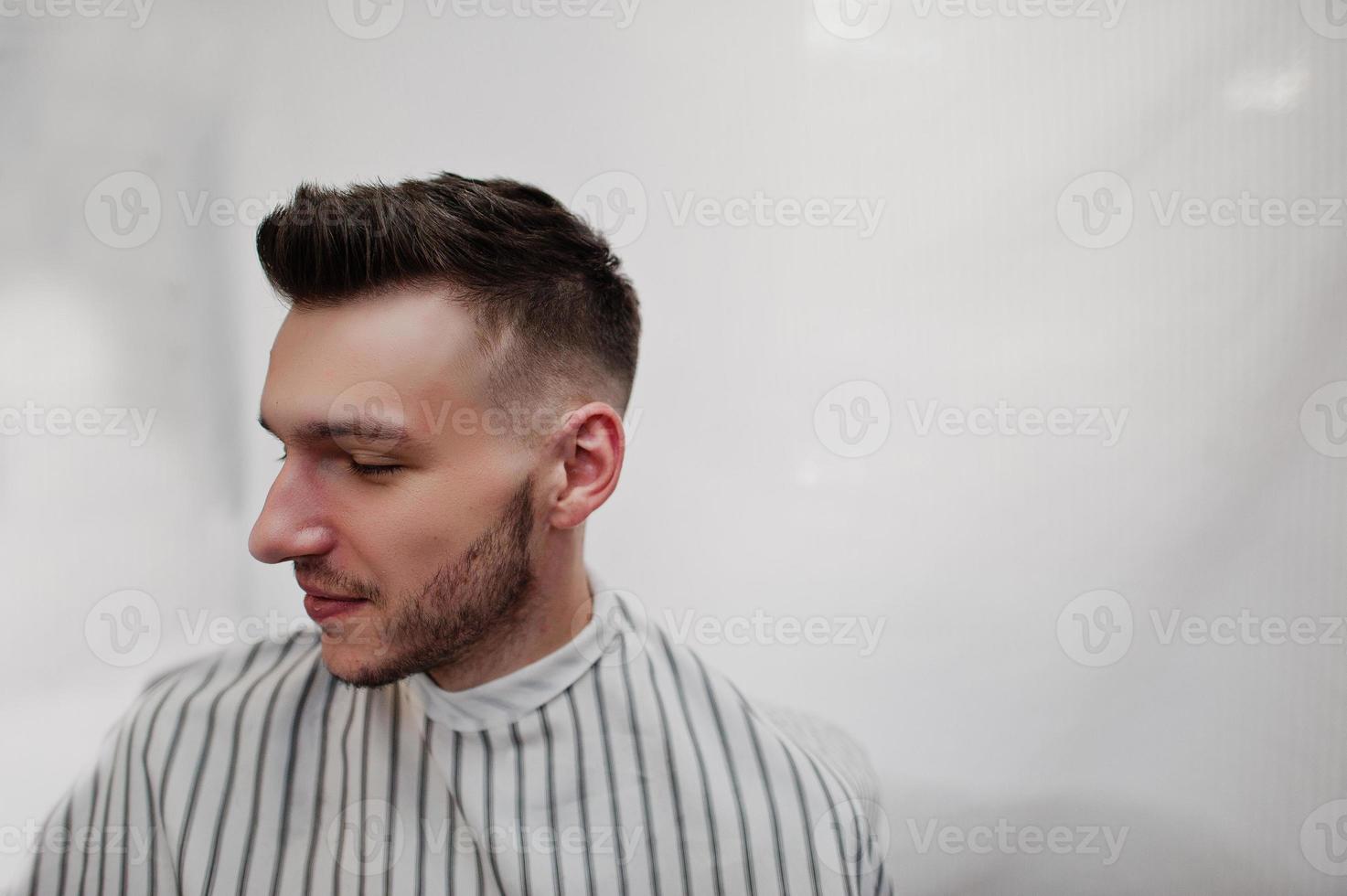 närbild huvudet av ung skäggig man får frisyr på barbershop. frisörsjäl. foto