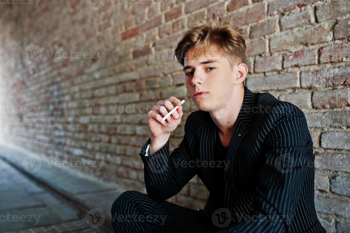 ung macho pojke bära på svart snygg jacka röka cigarett på gatorna. foto