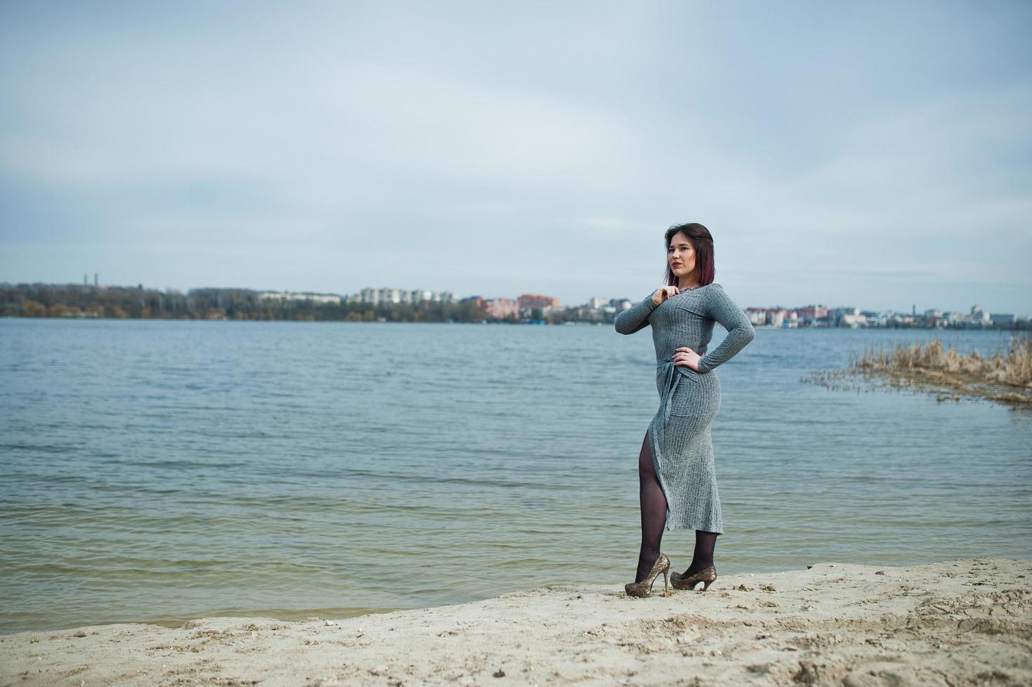 porträtt av brunett flicka i grå klänning bakgrund sjön. foto
