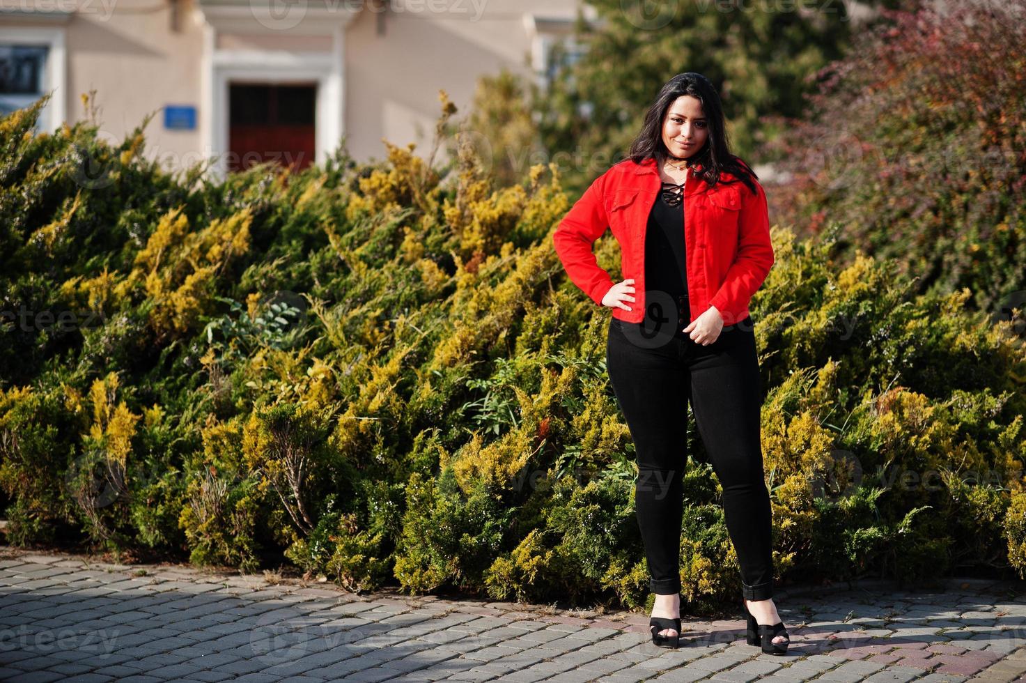 söt latino modell tjej från ecuador bär på svart och röd jacka poserade på gatan. foto