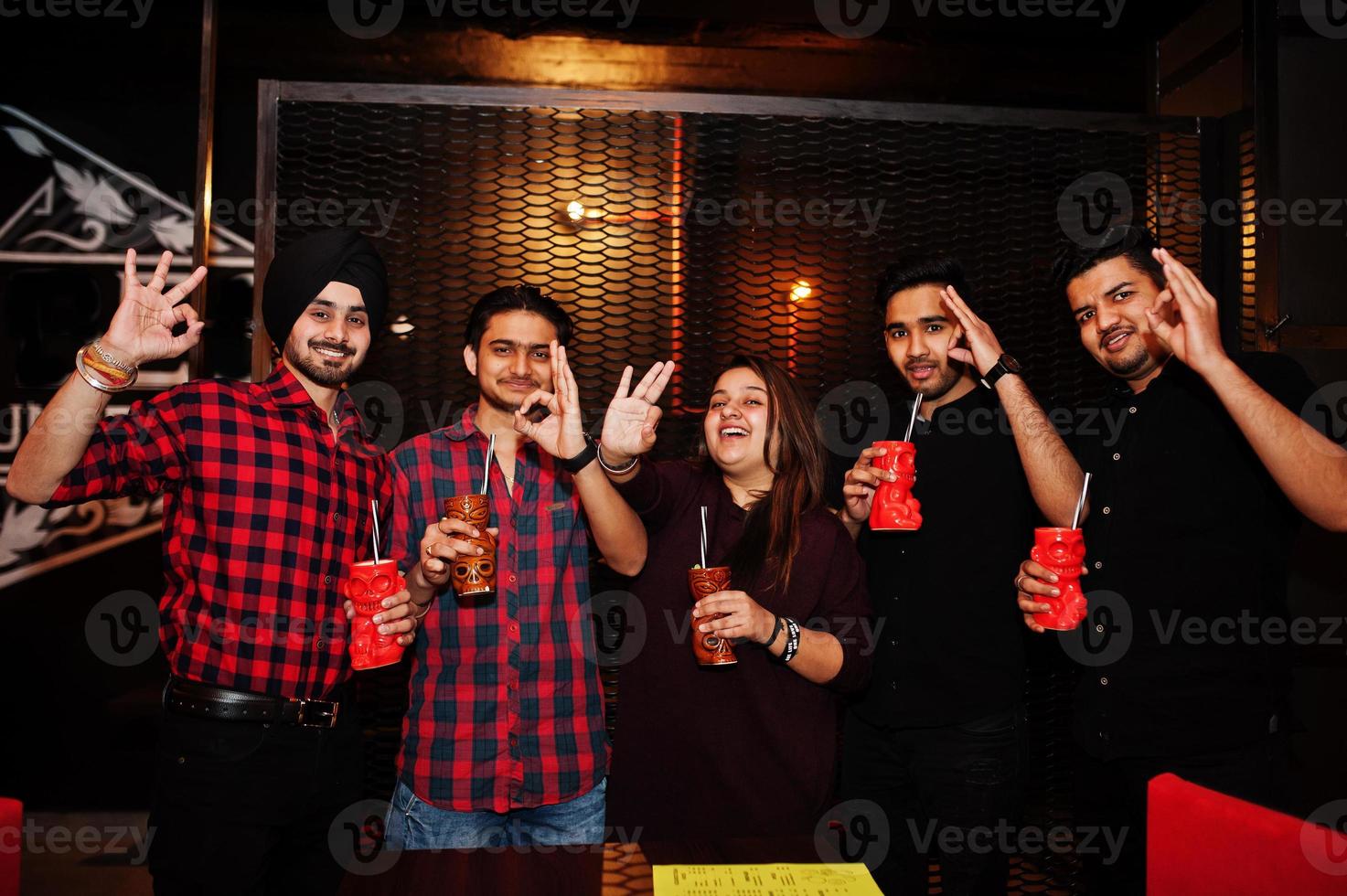 grupp indiska vänner har roligt och vila på nattklubb, dricker cocktails och visar ok fingrar tillsammans. foto