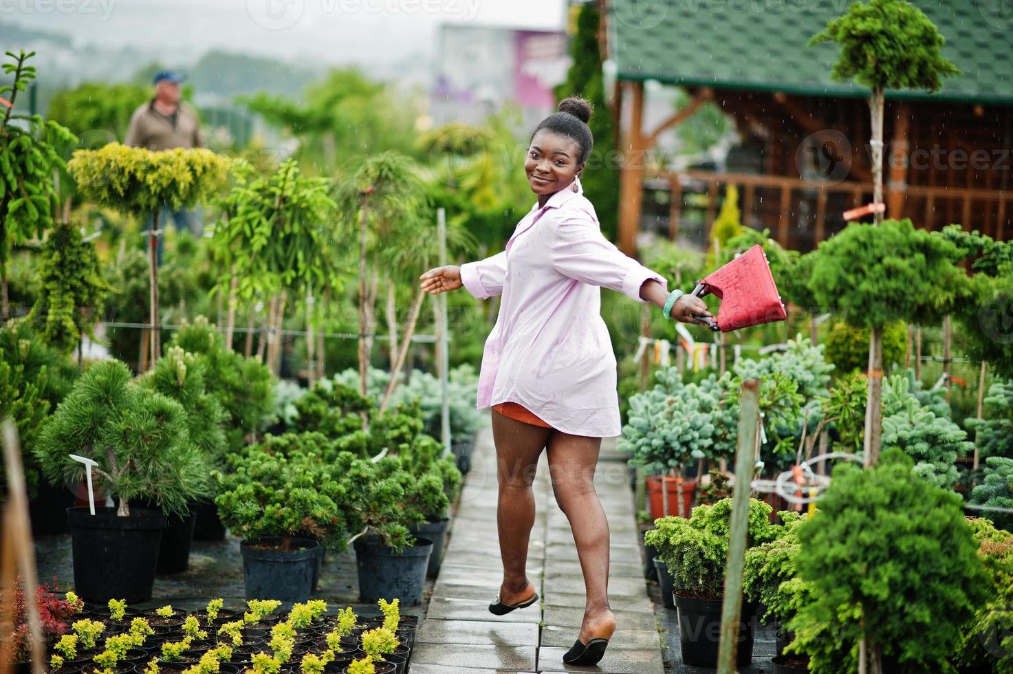 afrikansk kvinna i rosa stor skjorta poserade i trädgården med plantor. foto