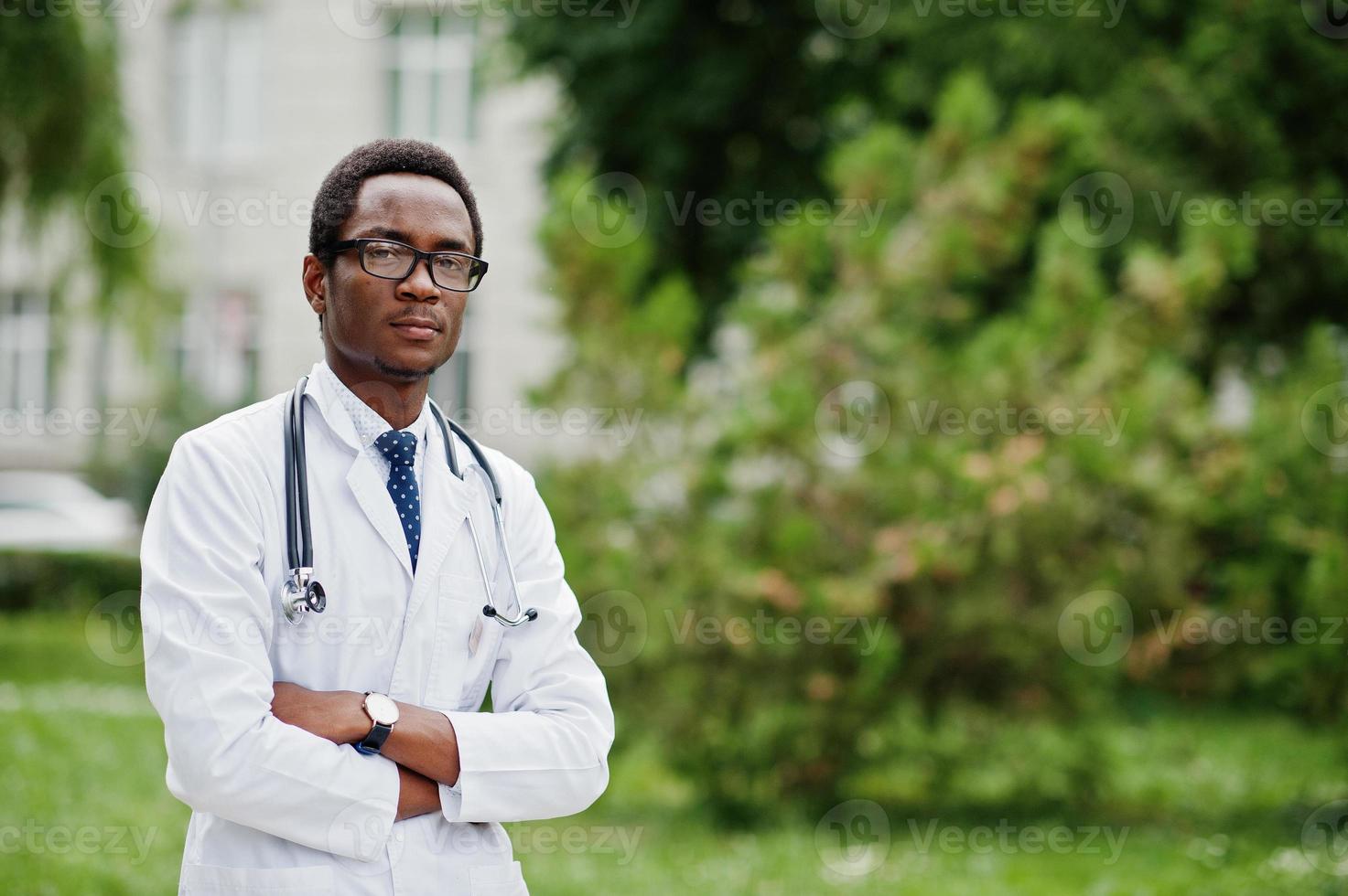 snygg afrikansk amerikansk läkare med stetoskop och labbrock, vid glasögon poserade utomhus. foto