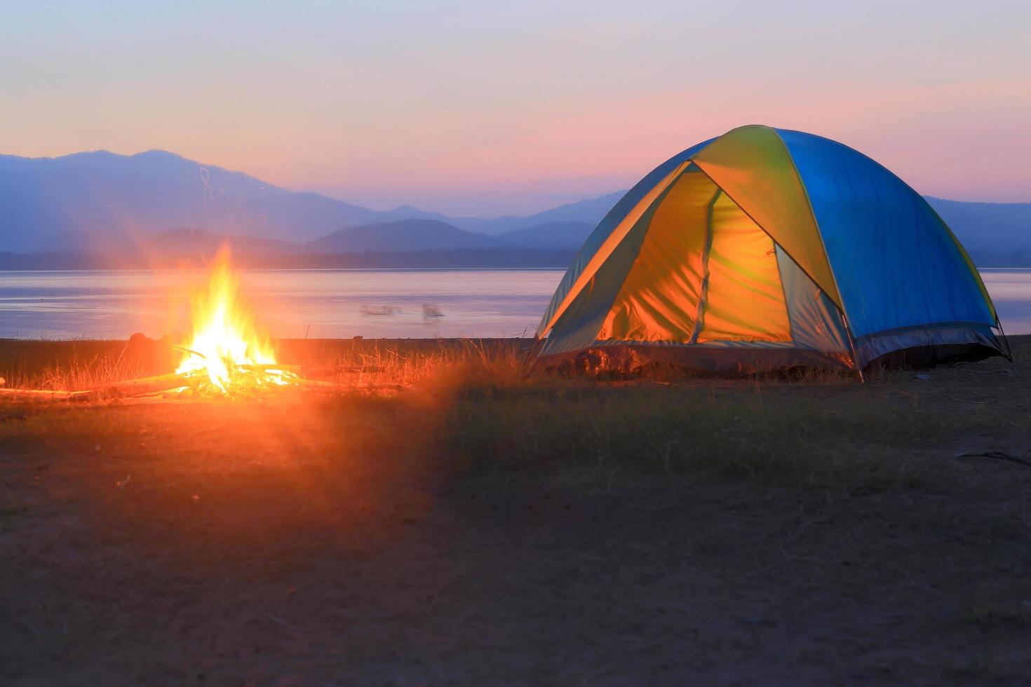 tält och lägereld vid solnedgången, bredvid sjön foto
