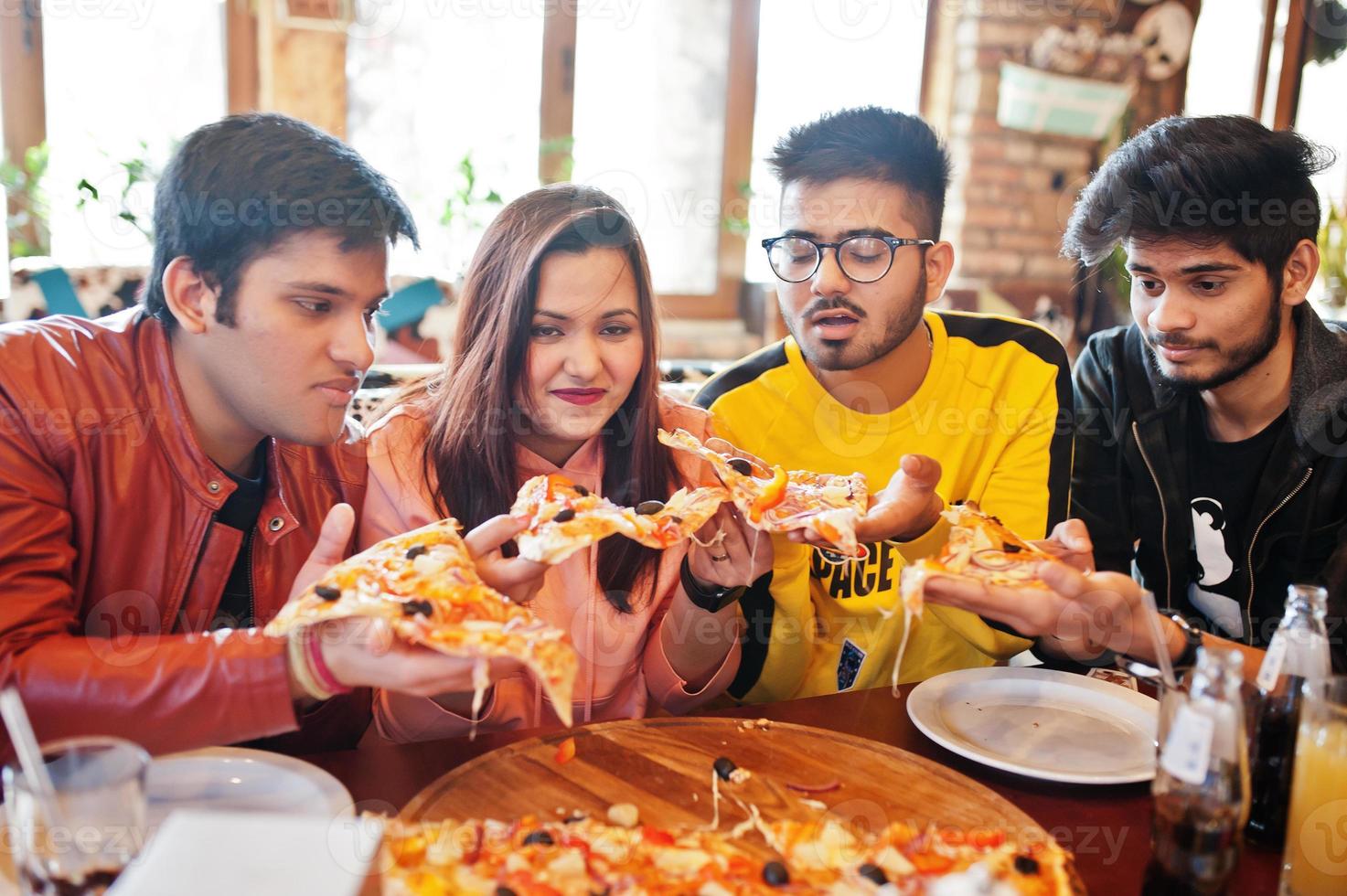 grupp asiatiska vänner som äter pizza under fest på pizzeria. glada indianer har roligt tillsammans, äter italiensk mat och sitter på soffan. foto