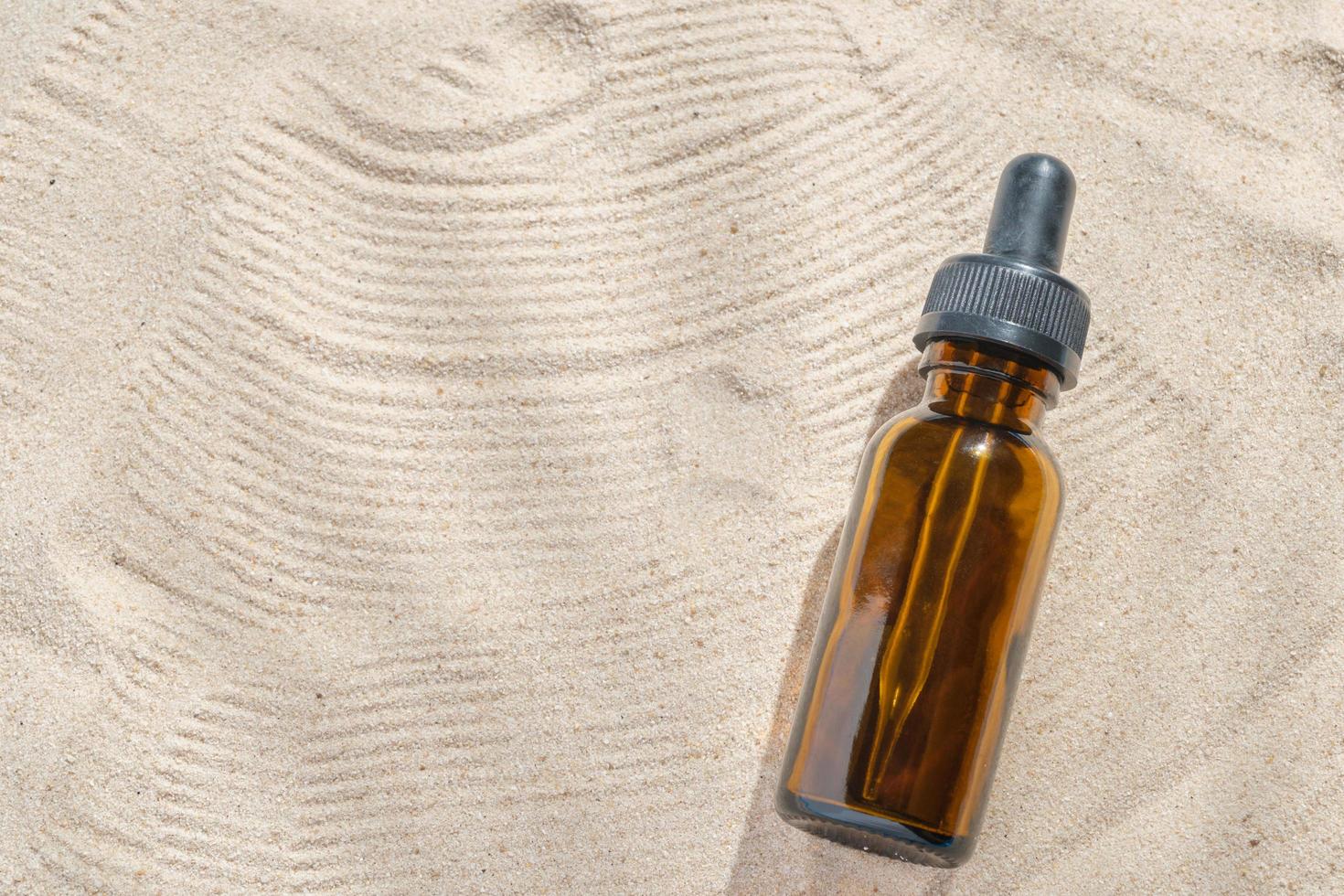 ansiktsserum av glasflaska med en pipett på en naturlig bakgrund med sand. eterisk olja för att återfukta kroppens hud. mockup av skönhetsmode kosmetisk flaska dropper produkt med hudvård koncept. foto