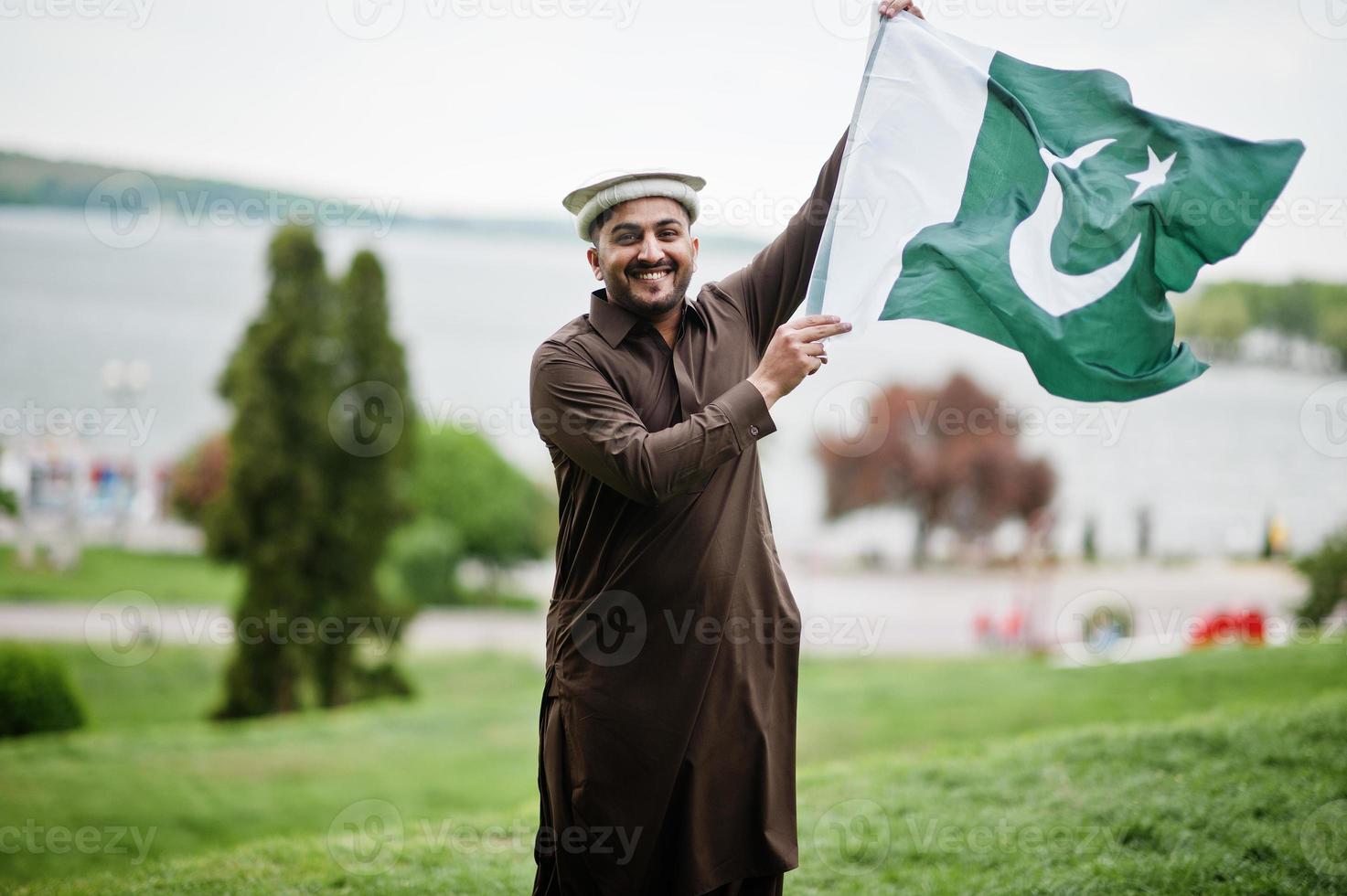 pakistanska pathan man bär traditionella kläder håller pakistanska flaggan. foto