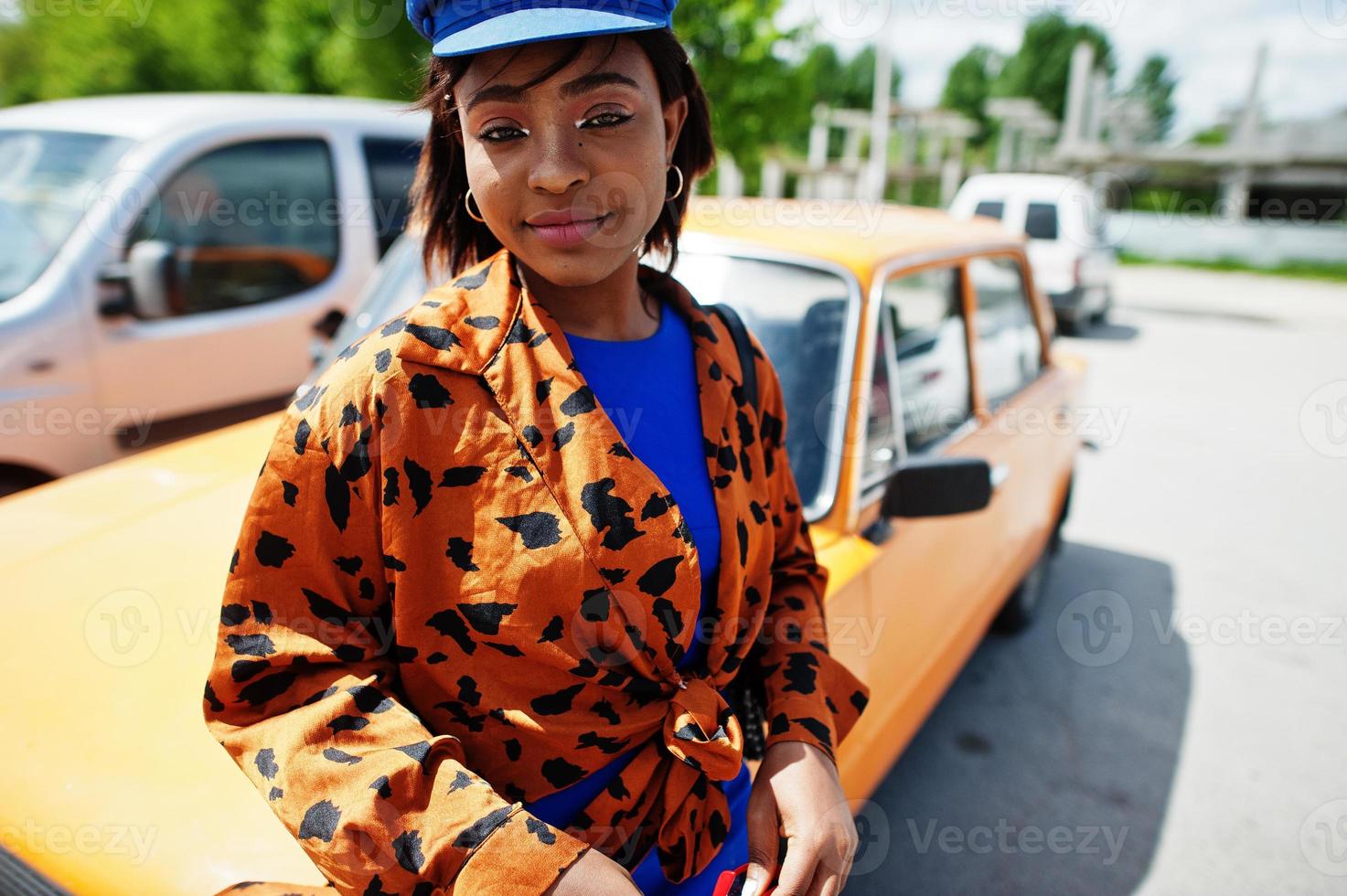 vacker afrikansk amerikansk dam med solglasögon som står nära orange klassisk retrobil. foto