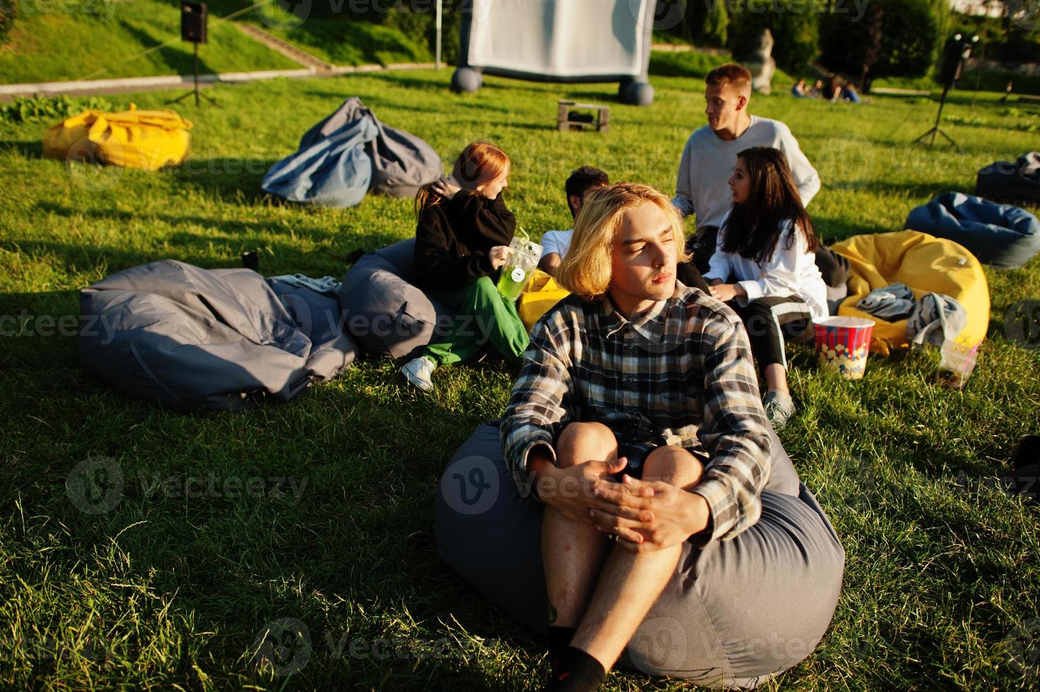 ung multietnisk grupp människor tittar på film på poff i utomhusbio. närbild porträtt av rolig kille. foto