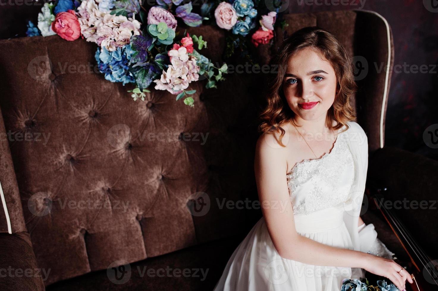 ganska ung tjej i vit klänning sitter på brun vintage soffa med blommor. foto