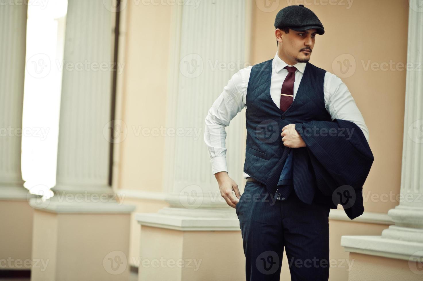 porträtt av retro engelsk arabisk affärsman från 1920-talet klädd i mörk kostym, slips och platt mössa. foto