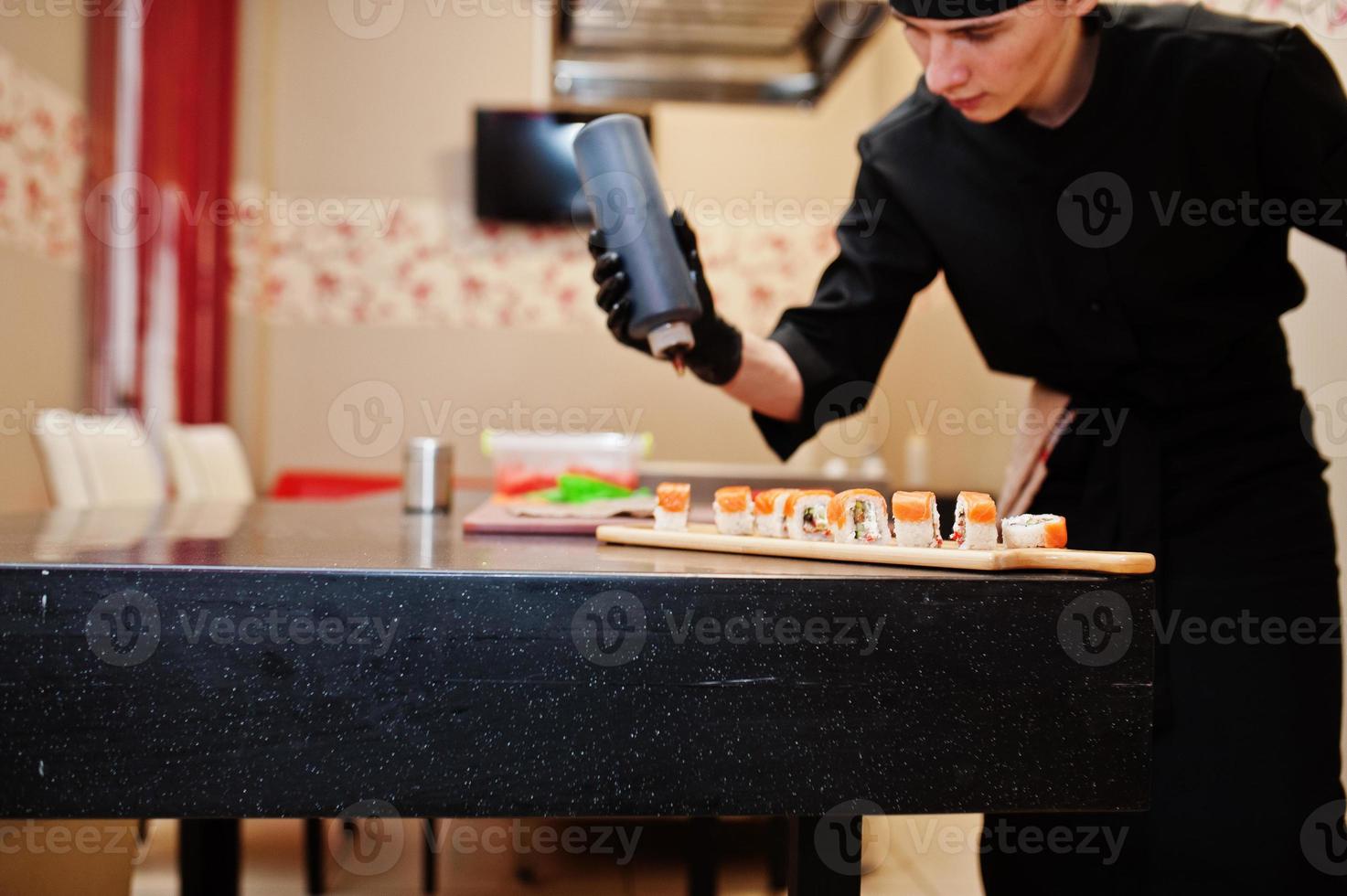 professionella kockkläder i svart gör sushi och rullar i ett restaurangkök med japansk traditionell mat. foto