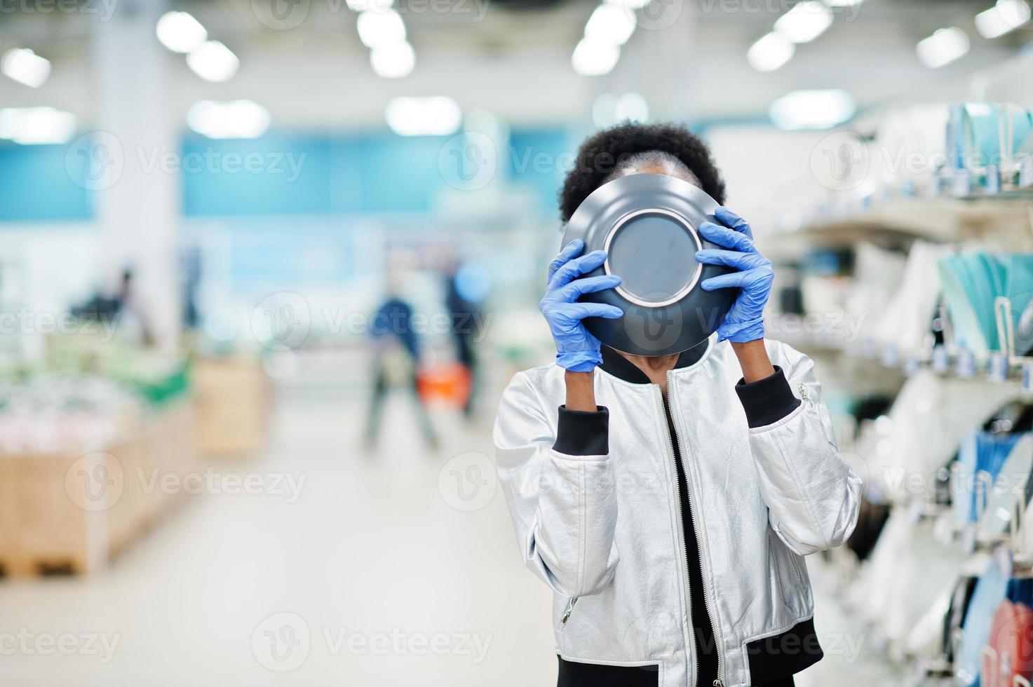 afrikansk kvinna som bär medicinsk engångsmask och handskar och shoppar i snabbköpet under utbrottet av coronavirus-pandemi. svart hona väljer skål vid epidemi tid. foto