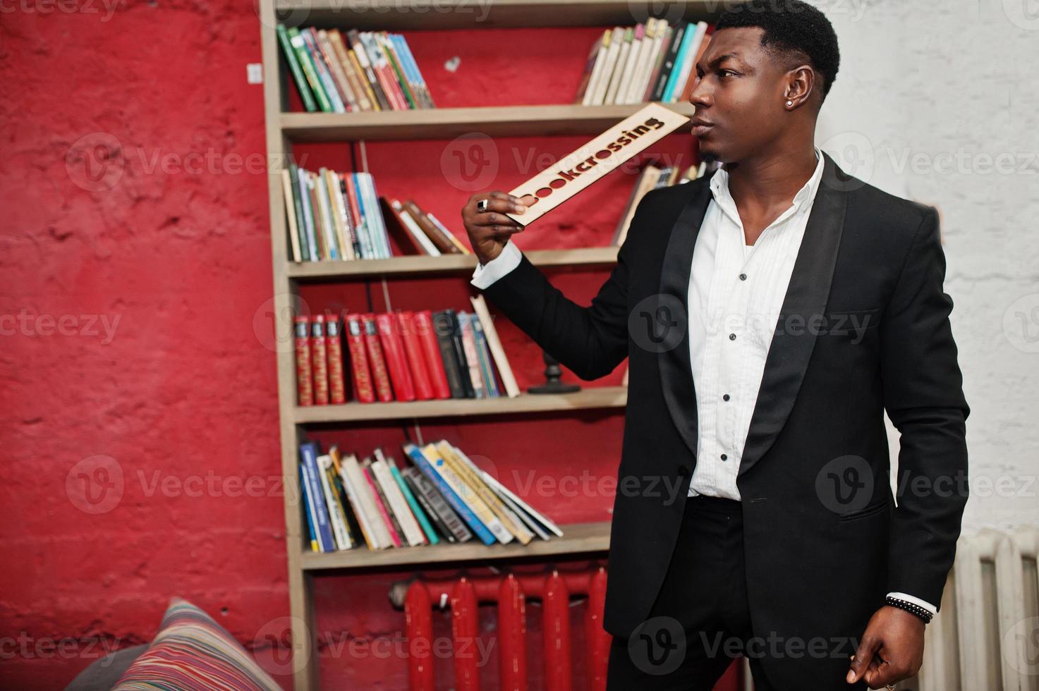 stark kraftfull afroamerikansk man i svart kostym mot bokhyllor i gratis böcker anti café. foto