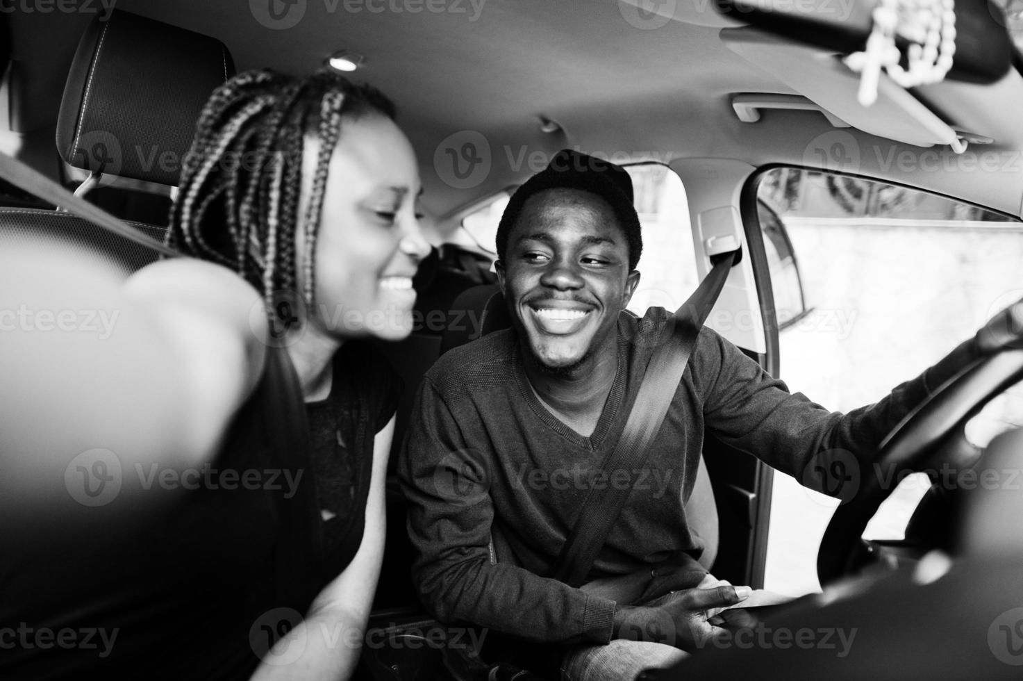 vackert ungt afroamerikanskt par som sitter på passagerarsätena fram medan stilig man kör bil. göra selfie tillsammans. foto