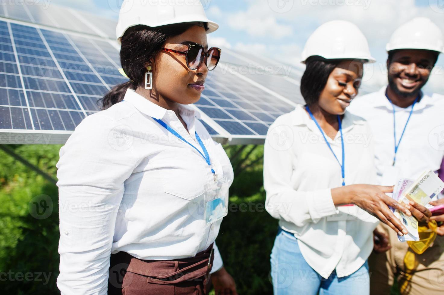 afrikansk amerikansk tekniker kontrollerar underhållet av solpanelerna. grupp om tre svarta ingenjörer som träffas på solstationen och gör en affär med pengar. foto