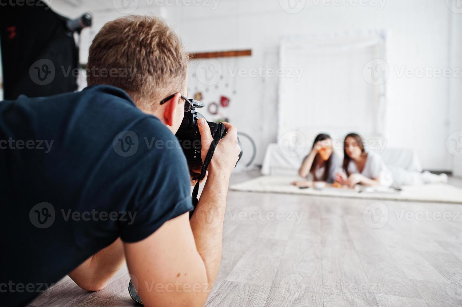 man fotograf fotograferar på studio tvillingflickor som äter pizza. professionell fotograf på jobbet. foto