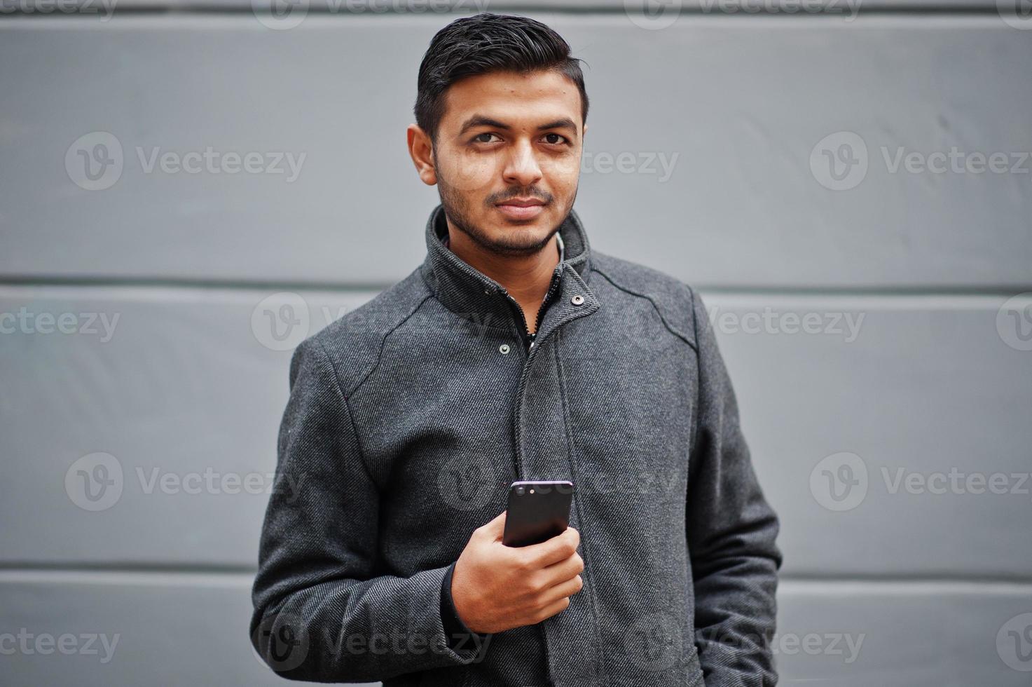 snygg indisk hinduisk man i grå rock poserade på gatan med mobiltelefon till hands. foto