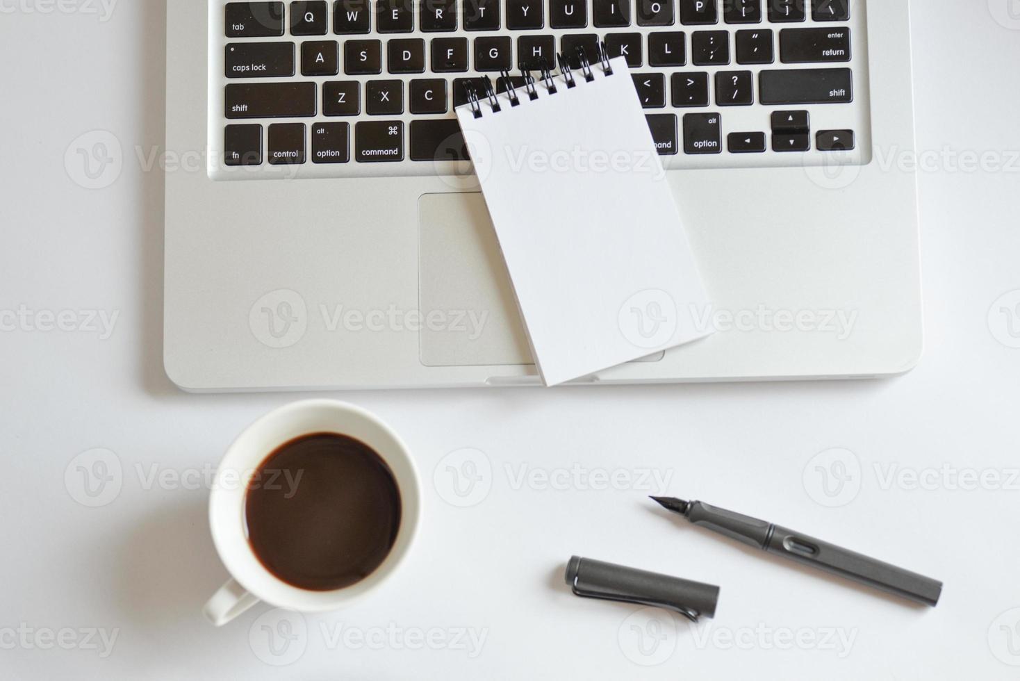 kaffekopp, spiral anteckningsbok, datortangentbord och penna på vitt foto