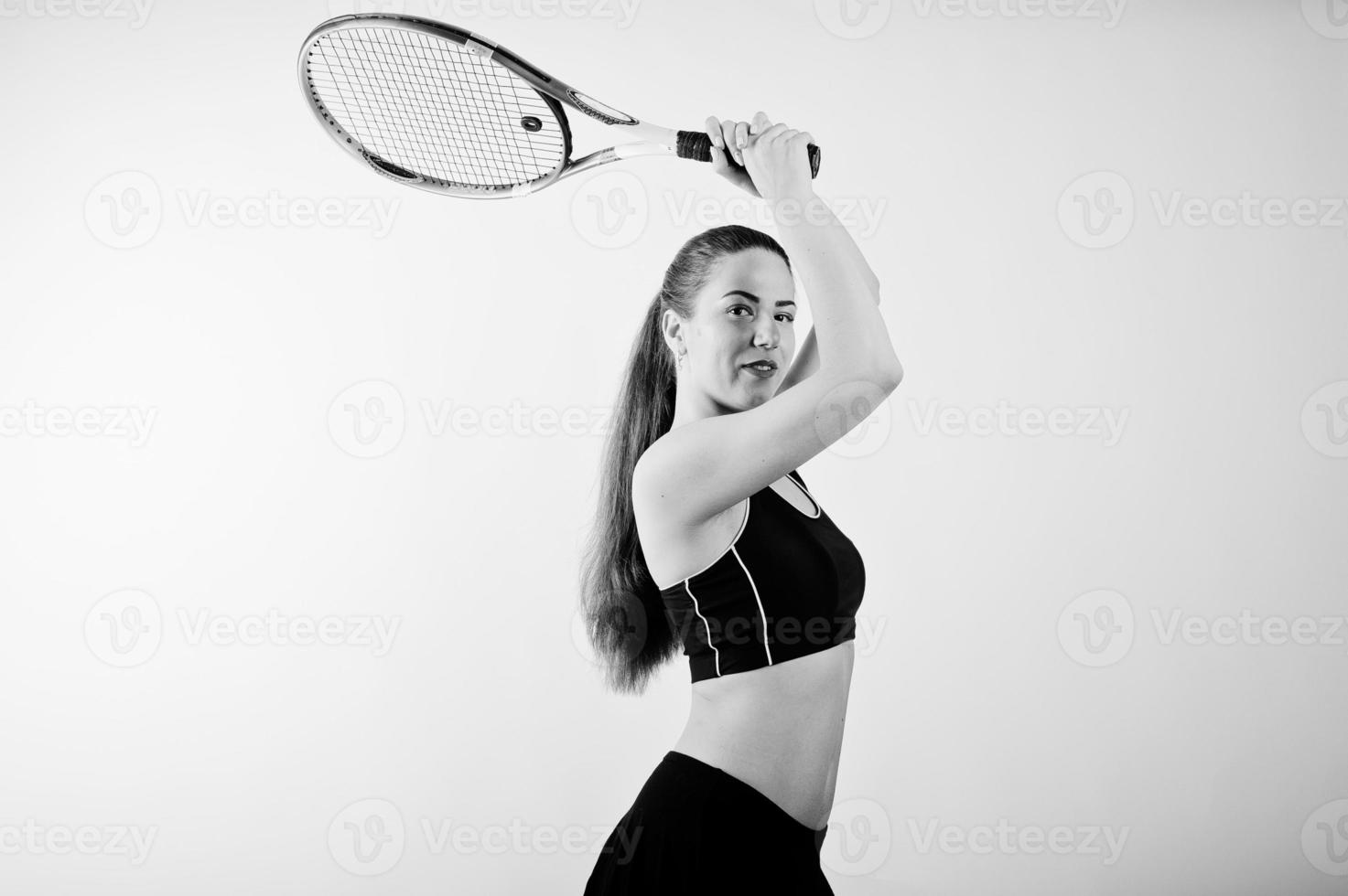 svart och vitt porträtt av vacker ung kvinna spelare i sportkläder håller tennisracket medan stående mot vit bakgrund. foto