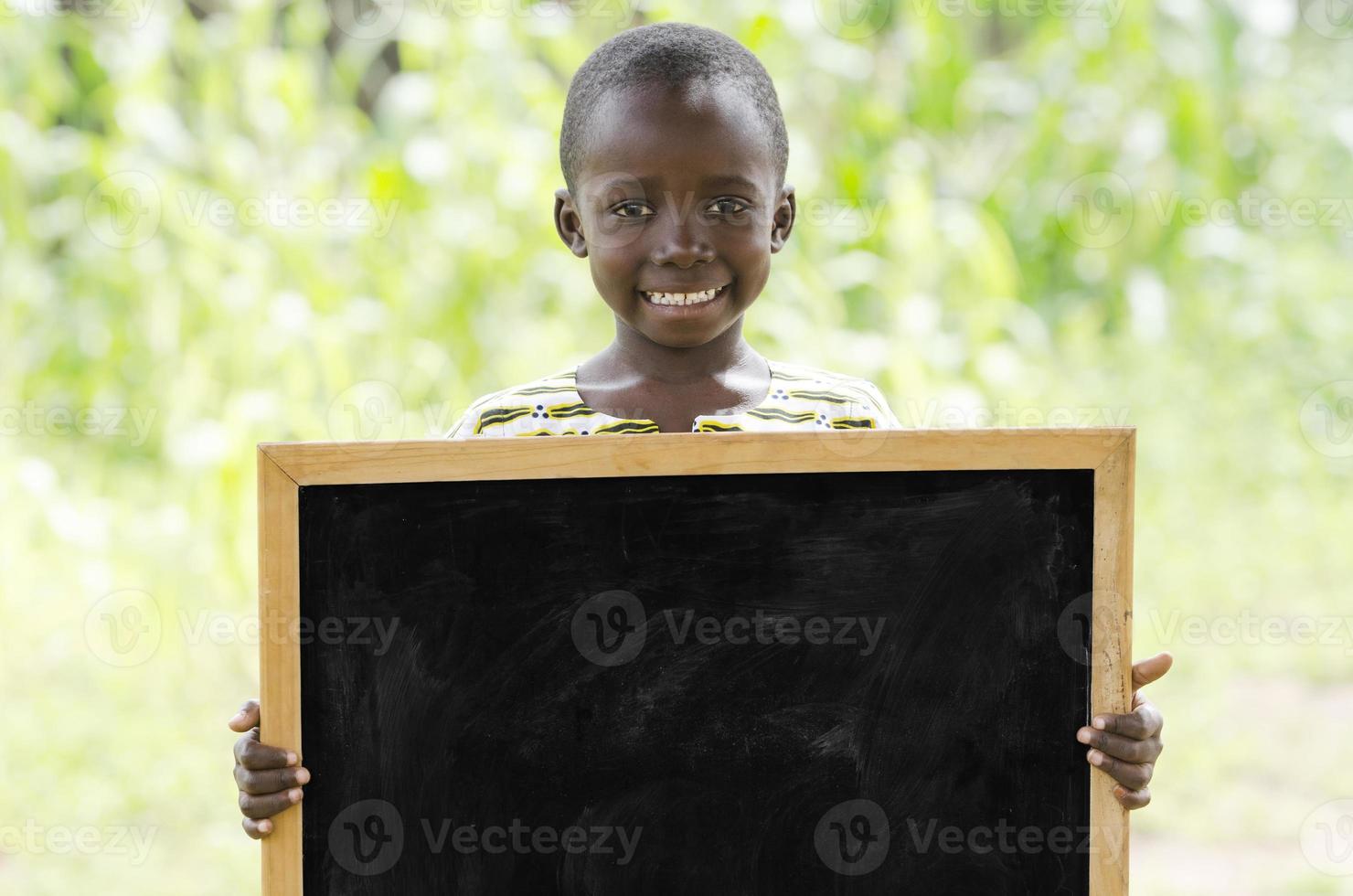 ung afrikansk pojke som håller svart tavla utomhus för en kommunikationssymbol foto