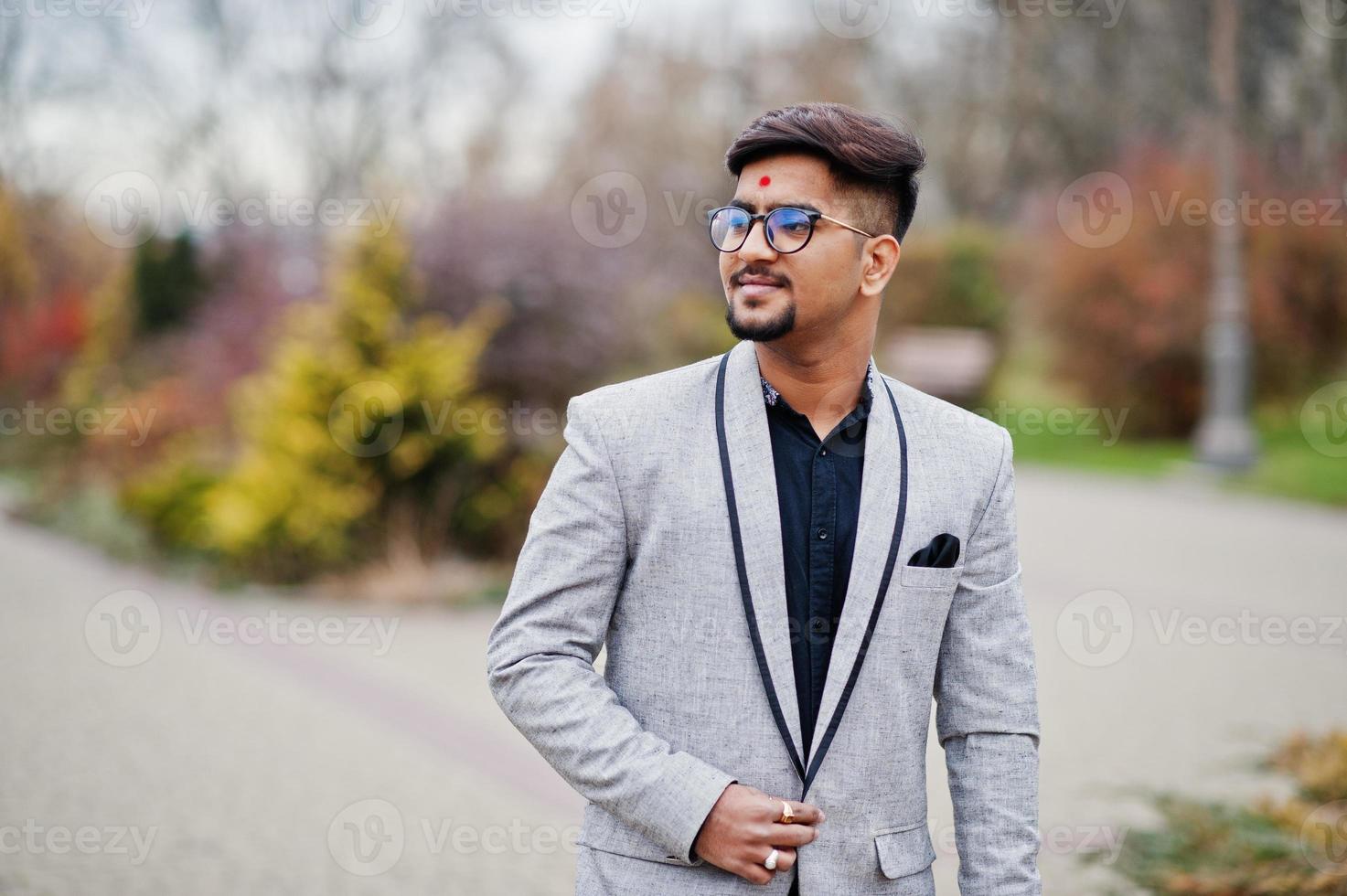 snygg indisk man med bindi på pannan och glasögon, bär på kostym poserade utomhus. foto