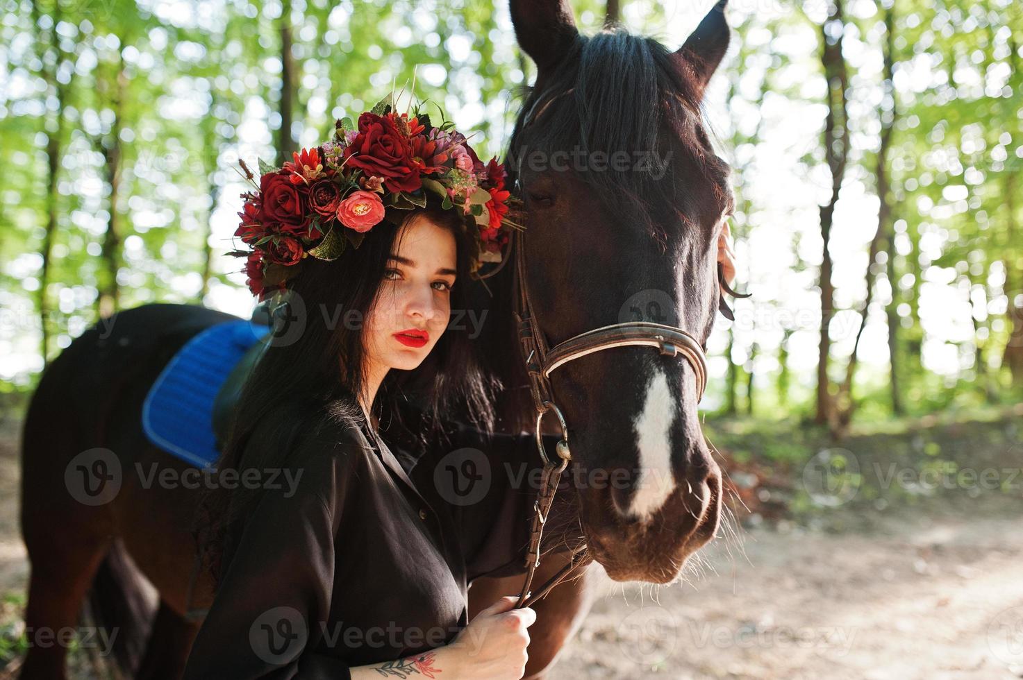 mystisk flicka i krans slitage i svart med häst i trä. foto