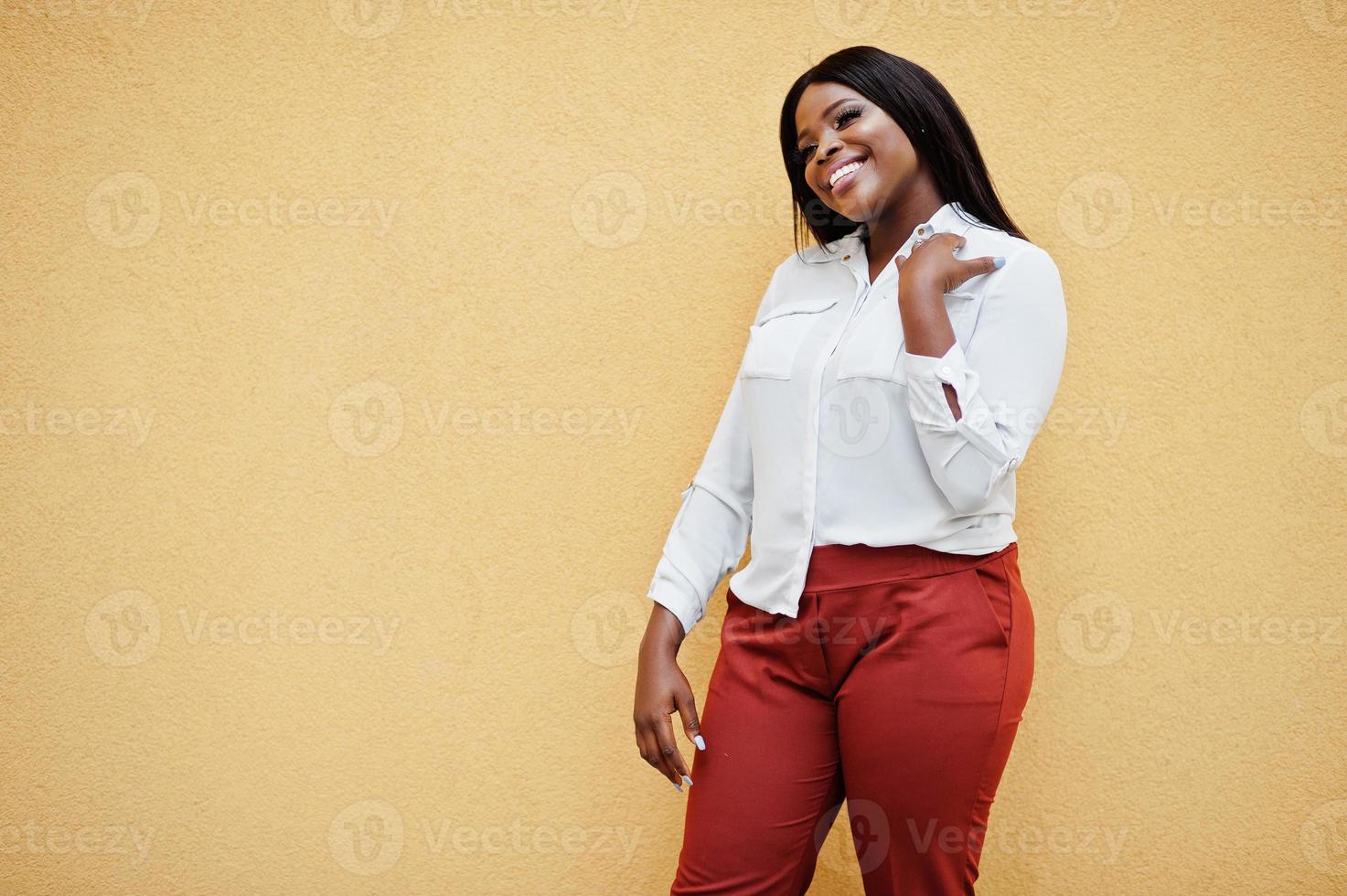 formellt klädd afrikansk amerikansk affärskvinna i vit blus och röda byxor isolerad på gul bakgrund. framgångsrik mörkhyad affärskvinna. foto