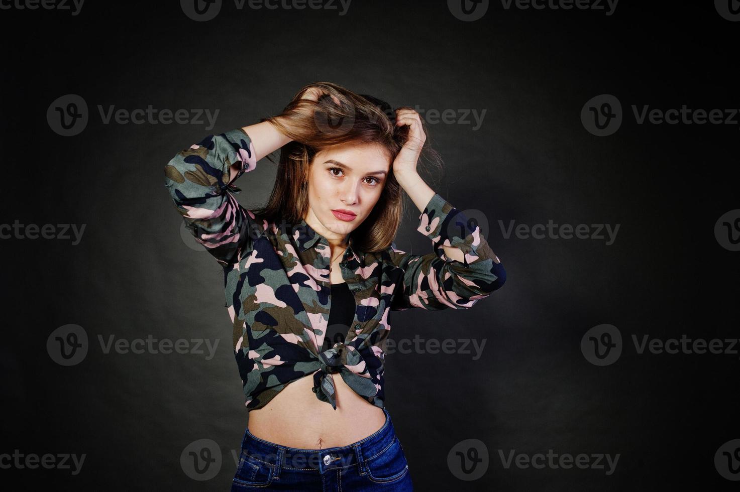 stilig brunett flicka bära militär skjorta och jeans, poserar på studio mot grå bakgrund. studio modell porträtt. foto