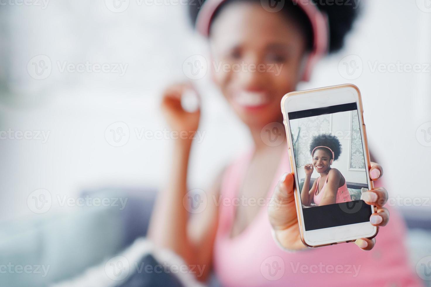 foto av skärmen mobiltelefon ung afroamerikansk kvinna sitter i soffan, lyssna på musik i hörlurar.