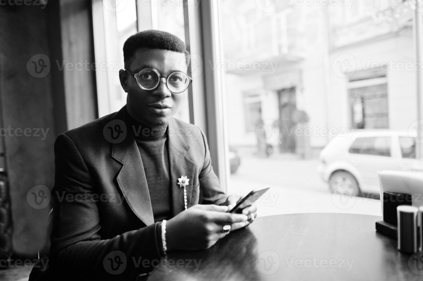 fashionabla afrikansk amerikansk man i kostym och glasögon håller mobiltelefon vid händerna poserade på café. foto