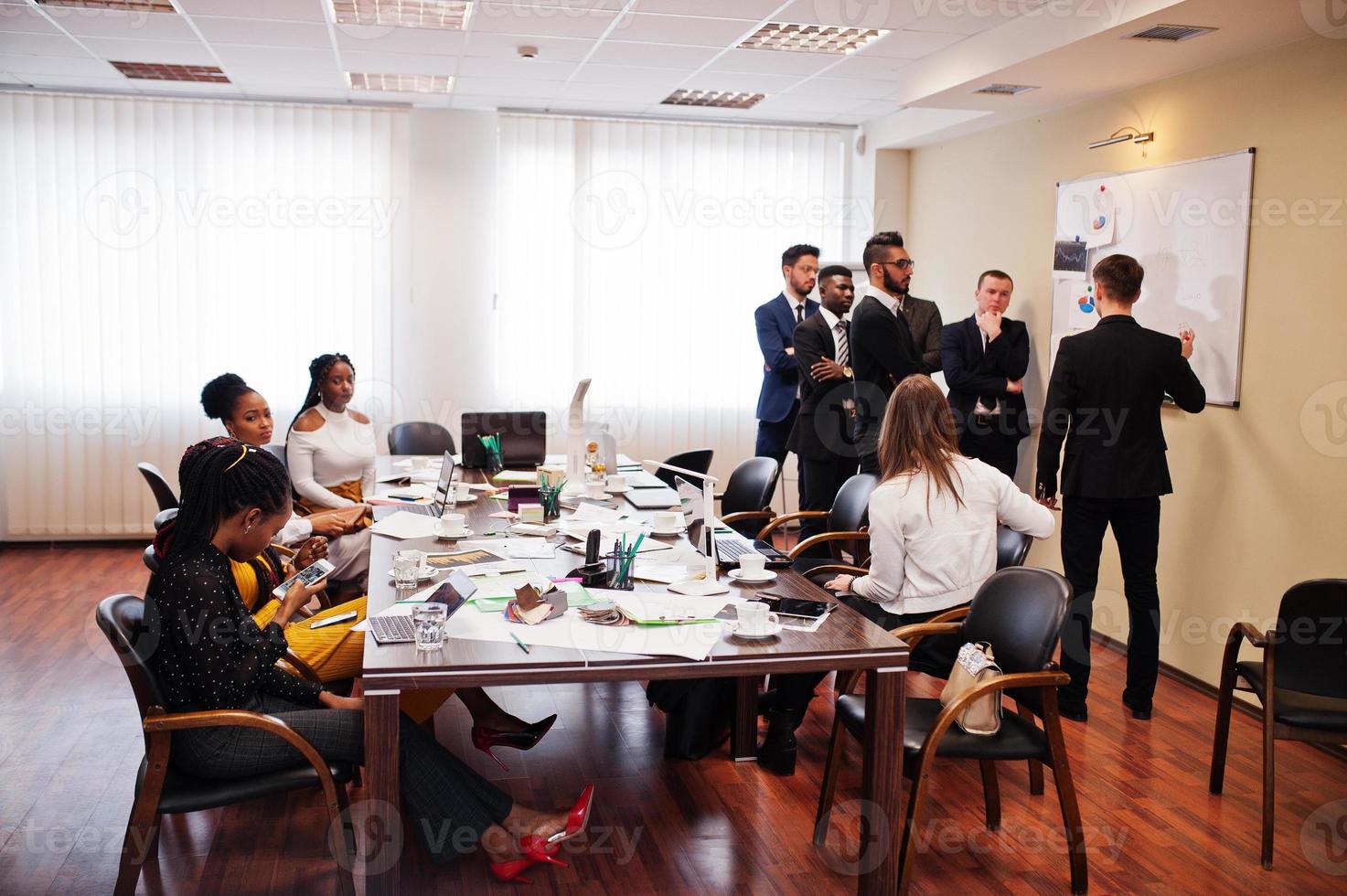 multiracial affärsteam som tar upp mötet runt styrelserumsbordet och skriver plan ombord. foto