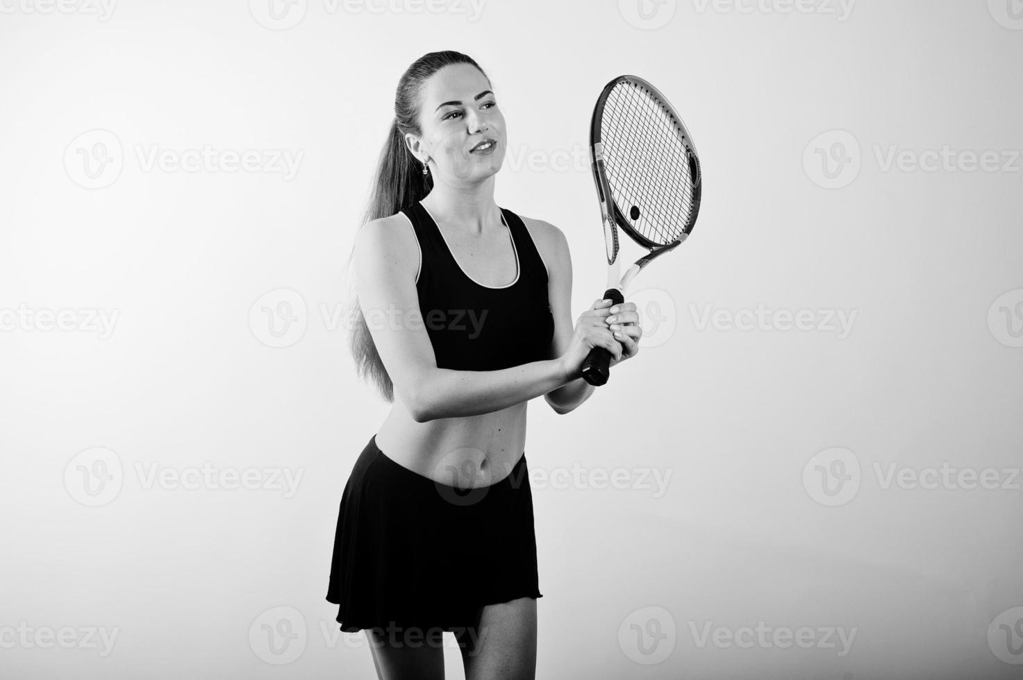 svart och vitt porträtt av vacker ung kvinna spelare i sportkläder håller tennisracket medan stående mot vit bakgrund. foto