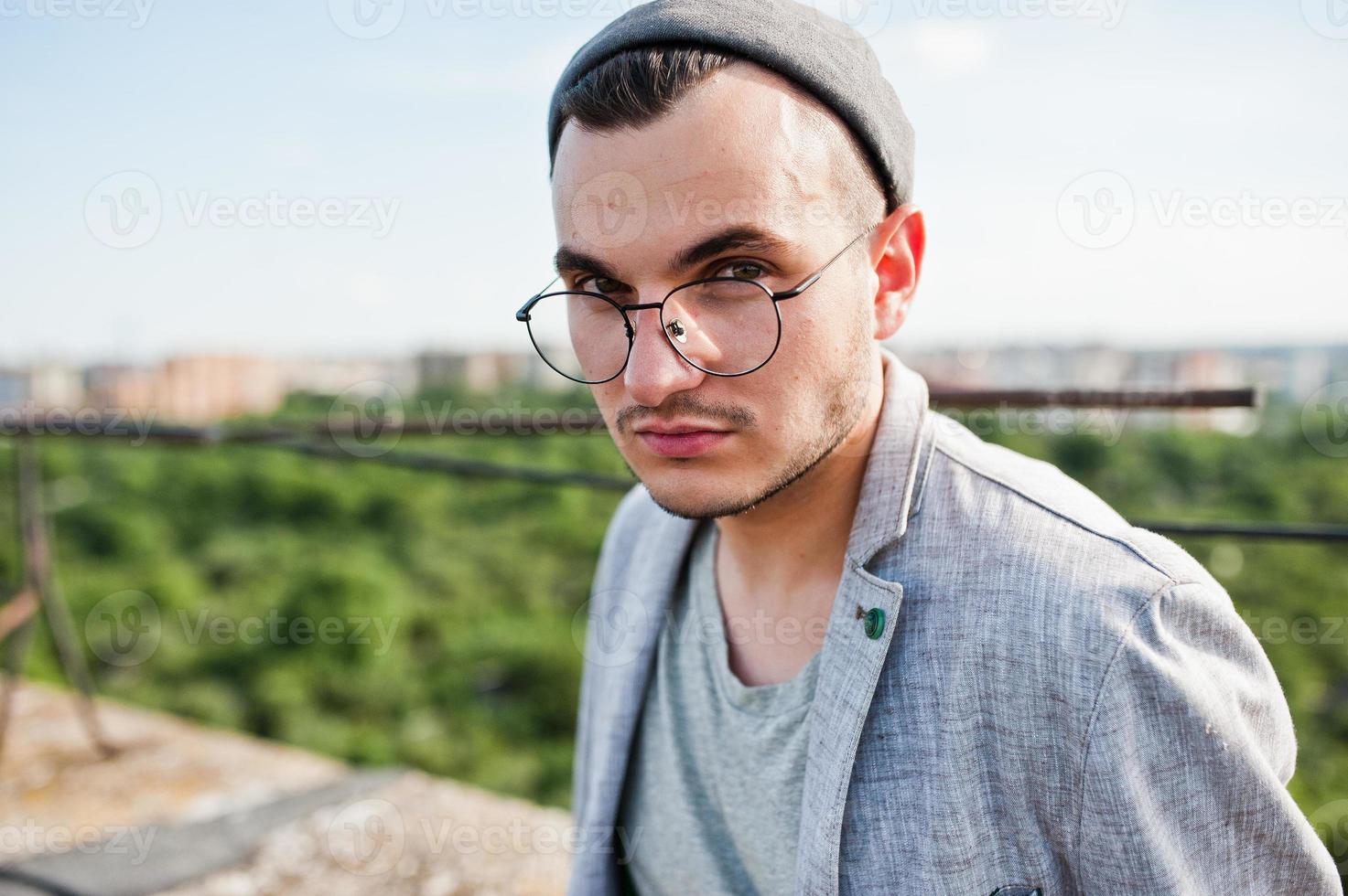 drömmare snygg macho man i grå kostym, hatt och glasögon poserade på taket. foto