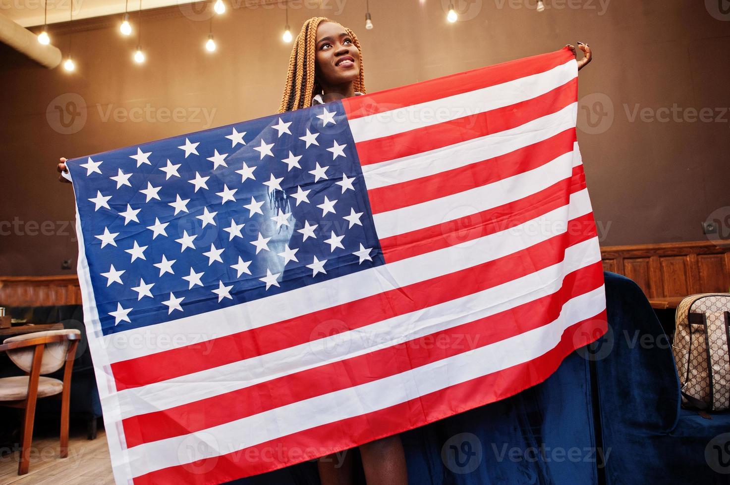 vacker afrikansk kvinna i snygga vardagskläder poserar med USA-flaggan vid händerna på kontoret. foto