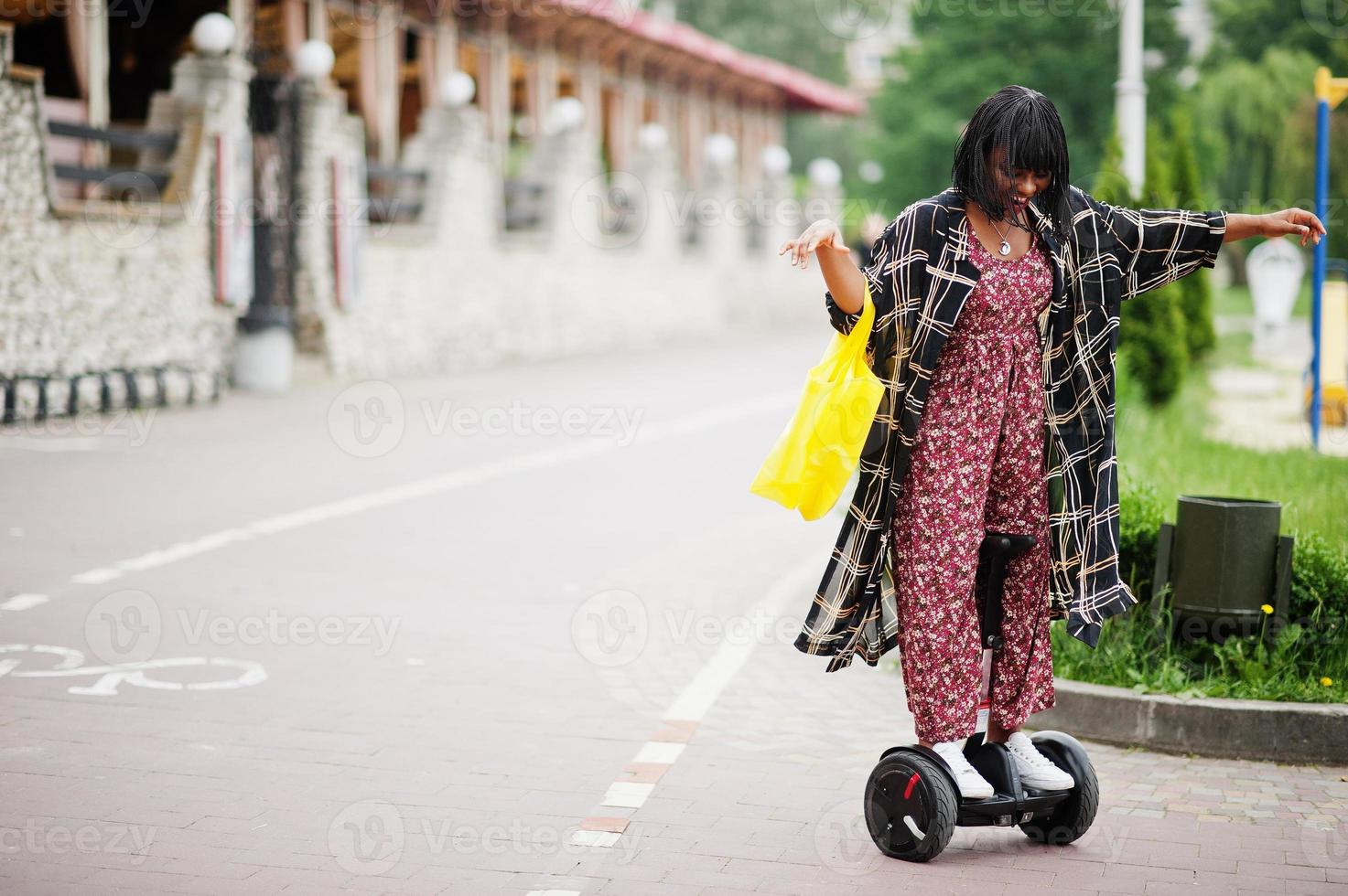 vacker afrikansk amerikansk kvinna som använder segway eller hoverboard. svart flicka med gul duk eco väskor återvinning symbol. foto