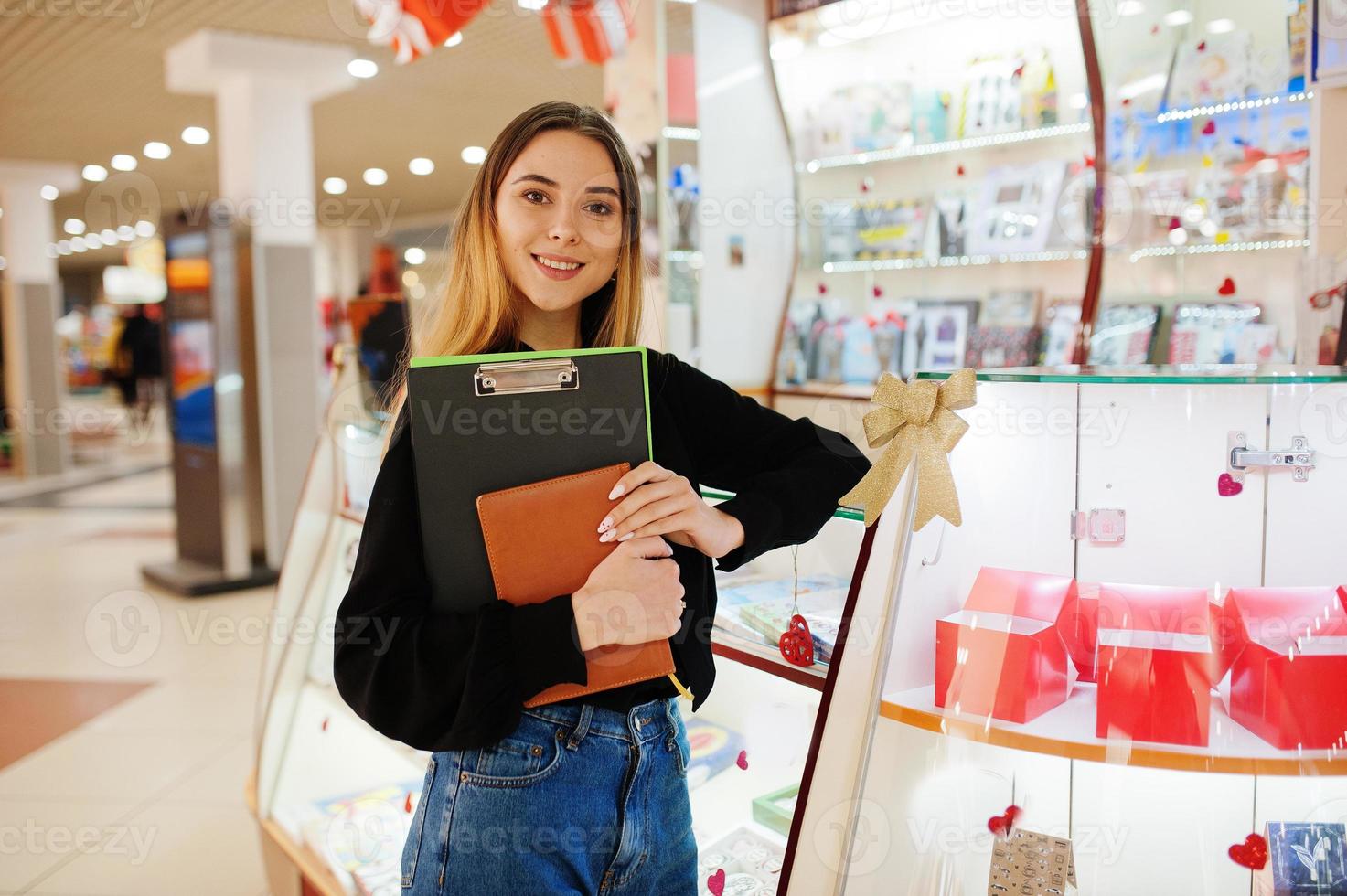 porträtt av ung kaukasisk kvinnlig kvinna säljare stå med urklipp och anteckningsbok. småföretag av godis souvenirbutik. foto