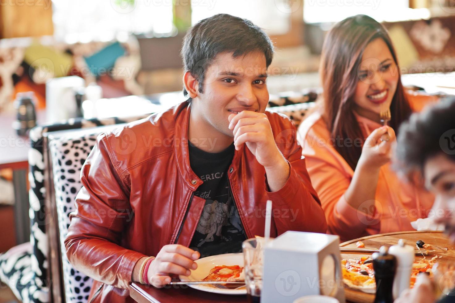 grupp asiatiska vänner som äter pizza under fest på pizzeria. glada indianer har roligt tillsammans, äter italiensk mat och sitter på soffan. foto