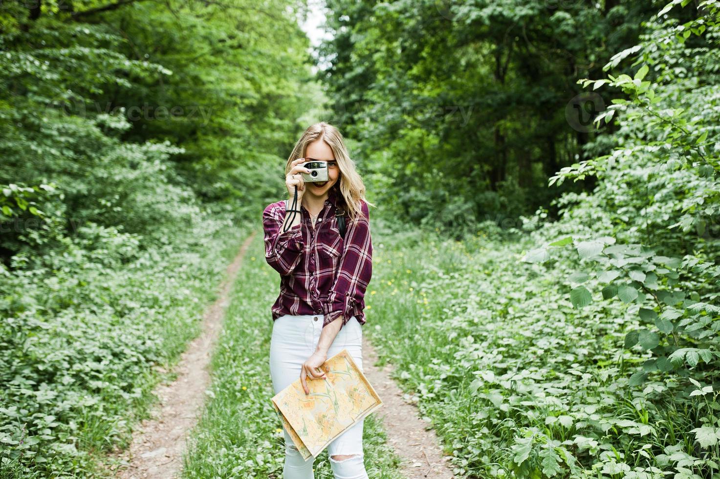 porträtt av en underbar ung flicka i tartanskjorta som tar bilder med kameran i skogen. foto