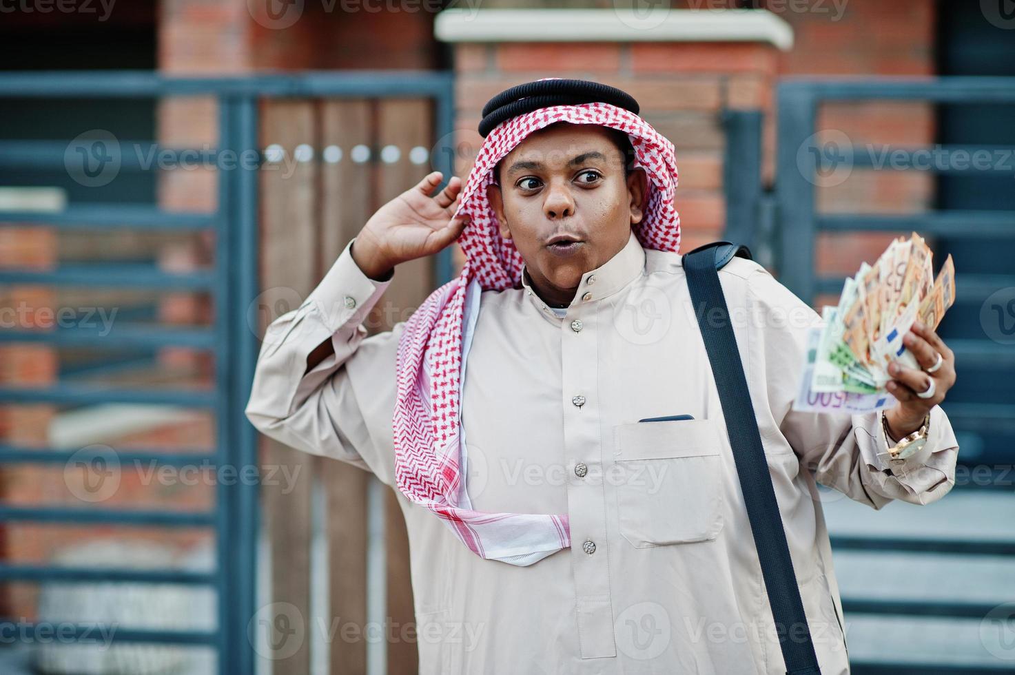 Mellanöstern arabisk affärsman poserade på gatan mot modern byggnad med svart handväska och europengar. foto