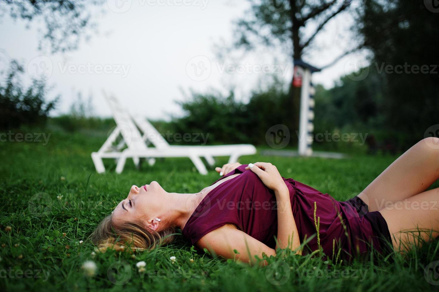 blond sensuell kvinna i röd marsala klänning liggande i det gröna gräset. foto